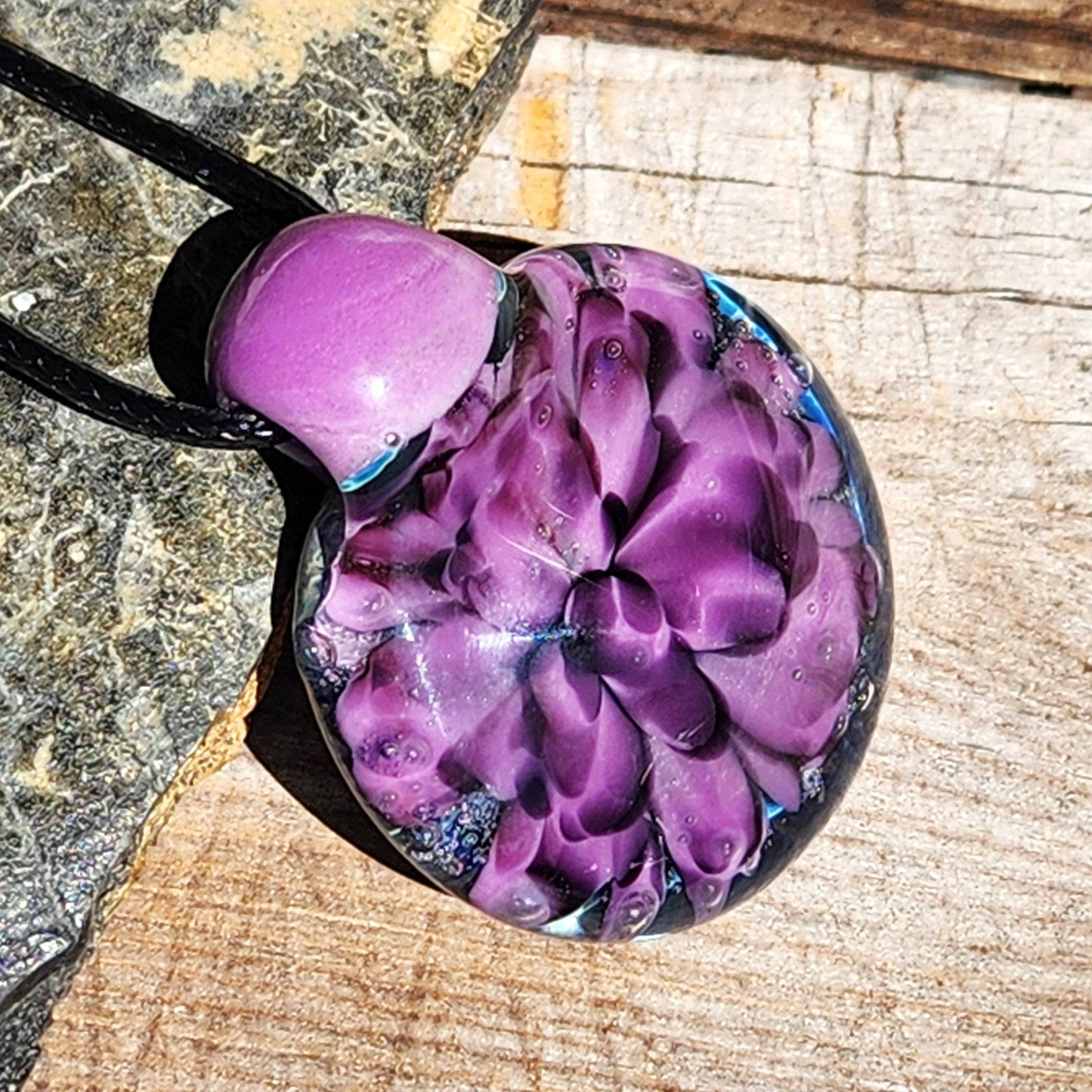 Sunlit view of handblown glass pendant with purple flower design, emphasizing the clarity and depth of borosilicate craftsmanship.