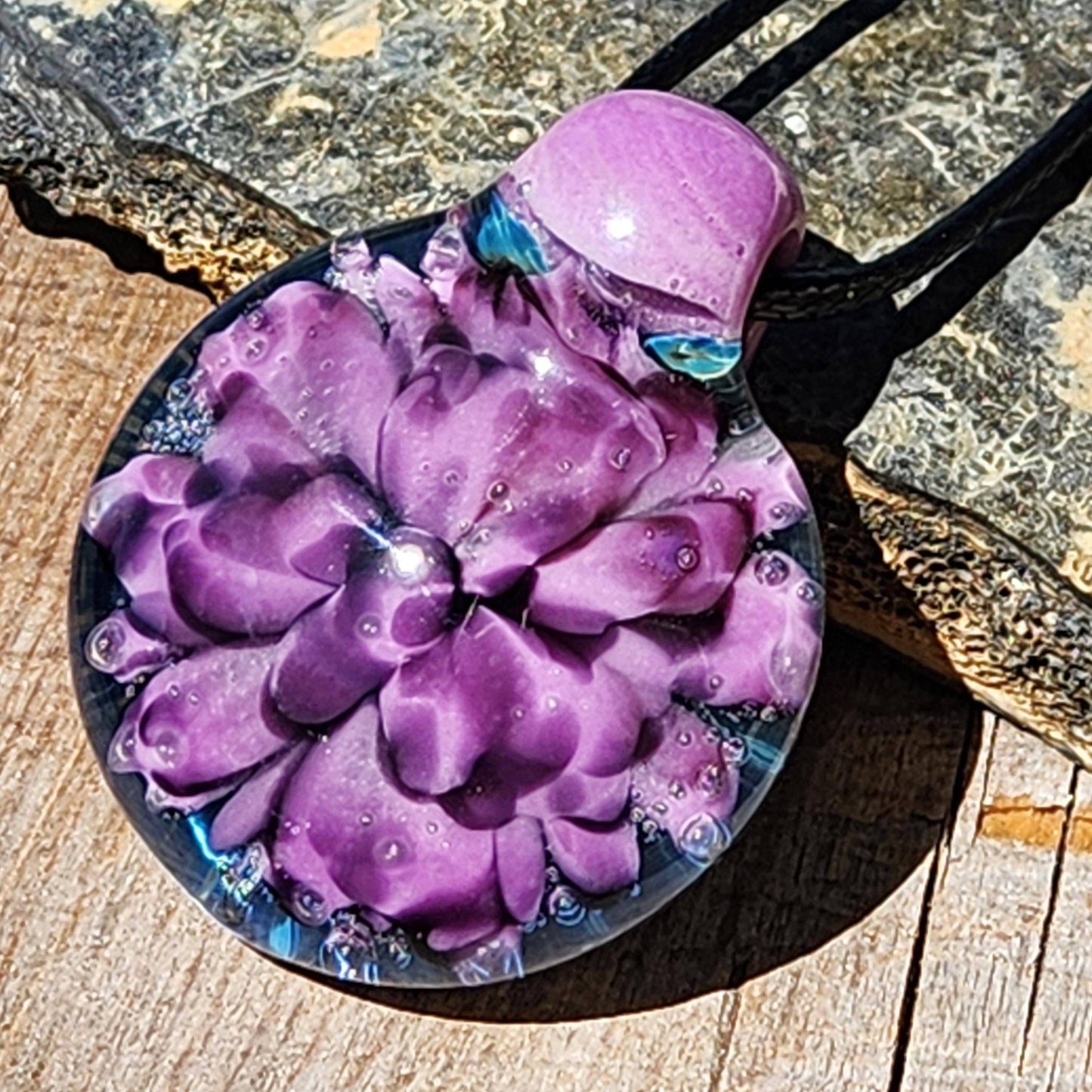 Close-up of handmade glass pendant with intricate purple flower encased in clear borosilicate glass. Artistic and one-of-a-kind jewelry charm.