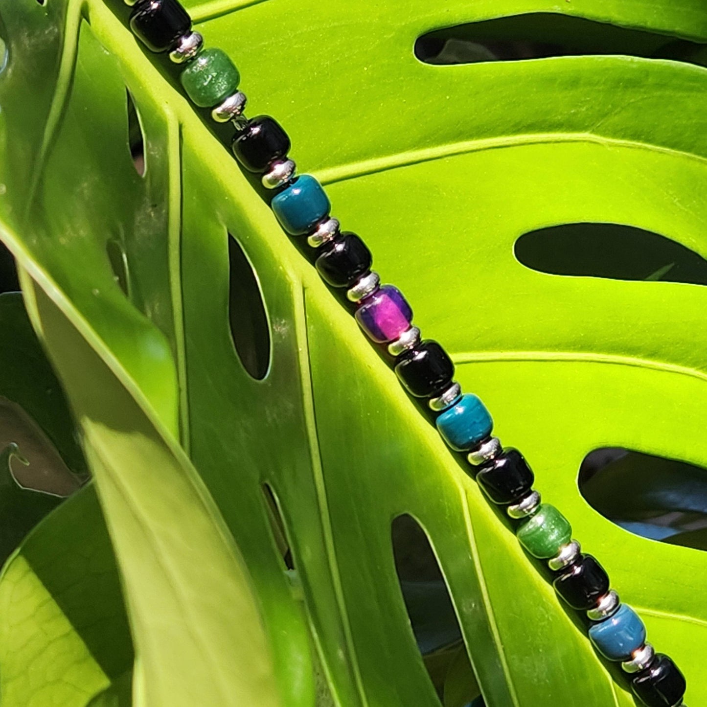 Boho Glass Beaded Bracelet with vibrant beads draped over a green monstera leaf, emphasizing its natural and handmade appeal.