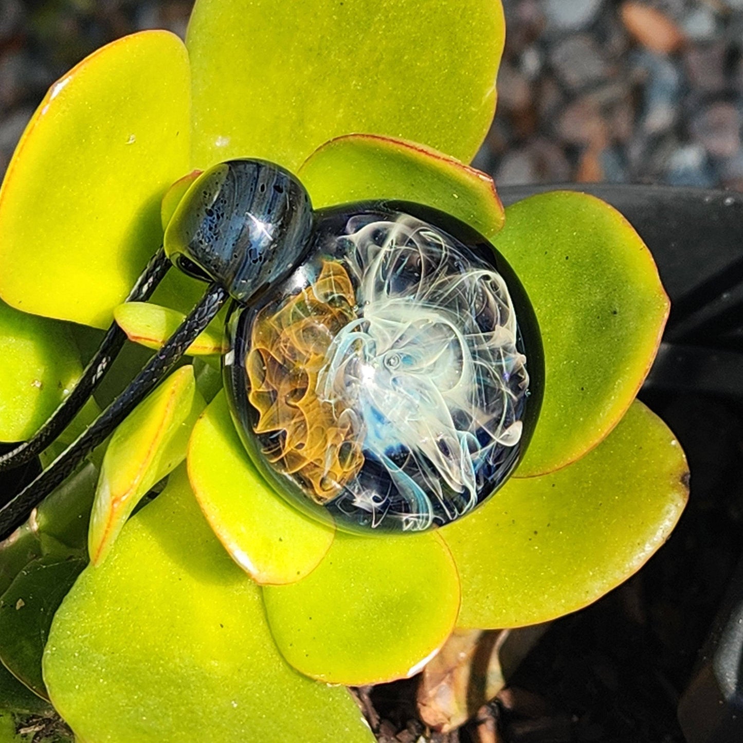 Gold & Silver Fumed Glass Pendant Necklace resting on succulent leaves. Unique handblown jewelry piece with blue, gold, and silver swirls.