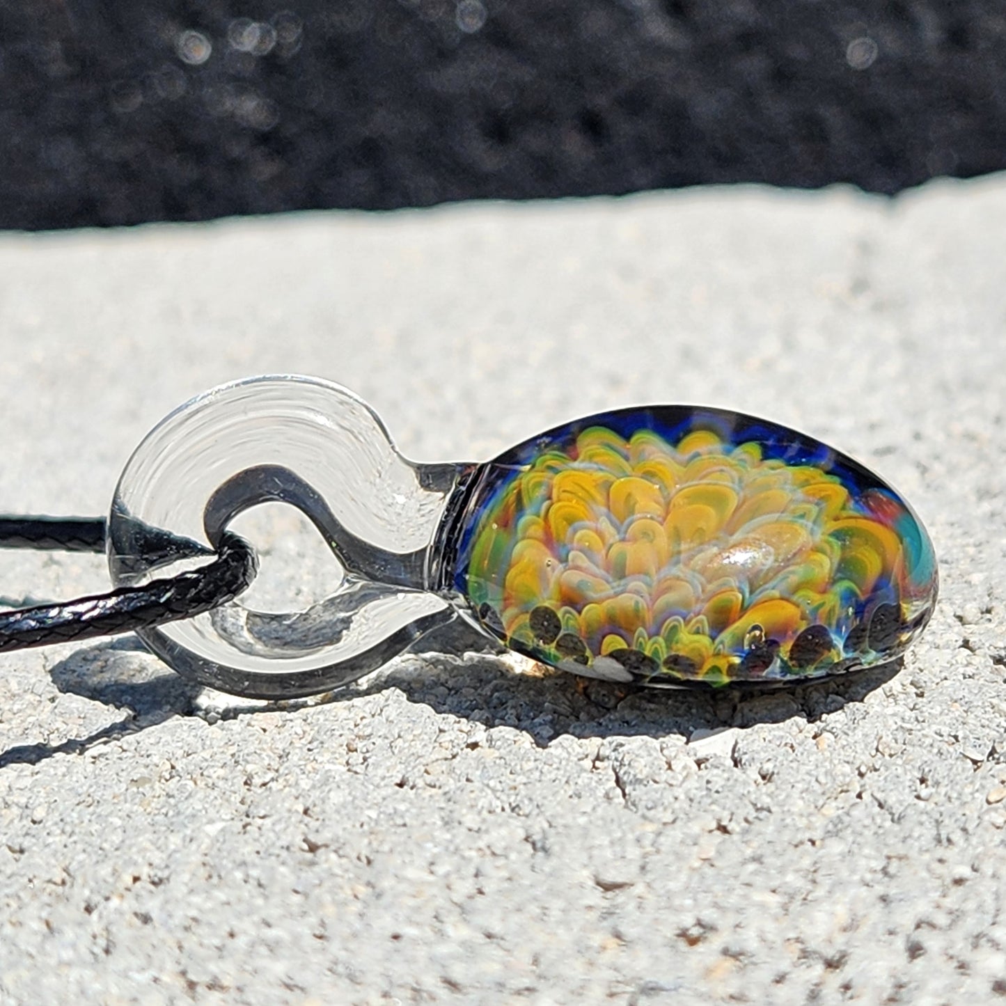 Green glass pendant necklace lying flat, displaying its vibrant yellow and blue flower design and clear glass loop.