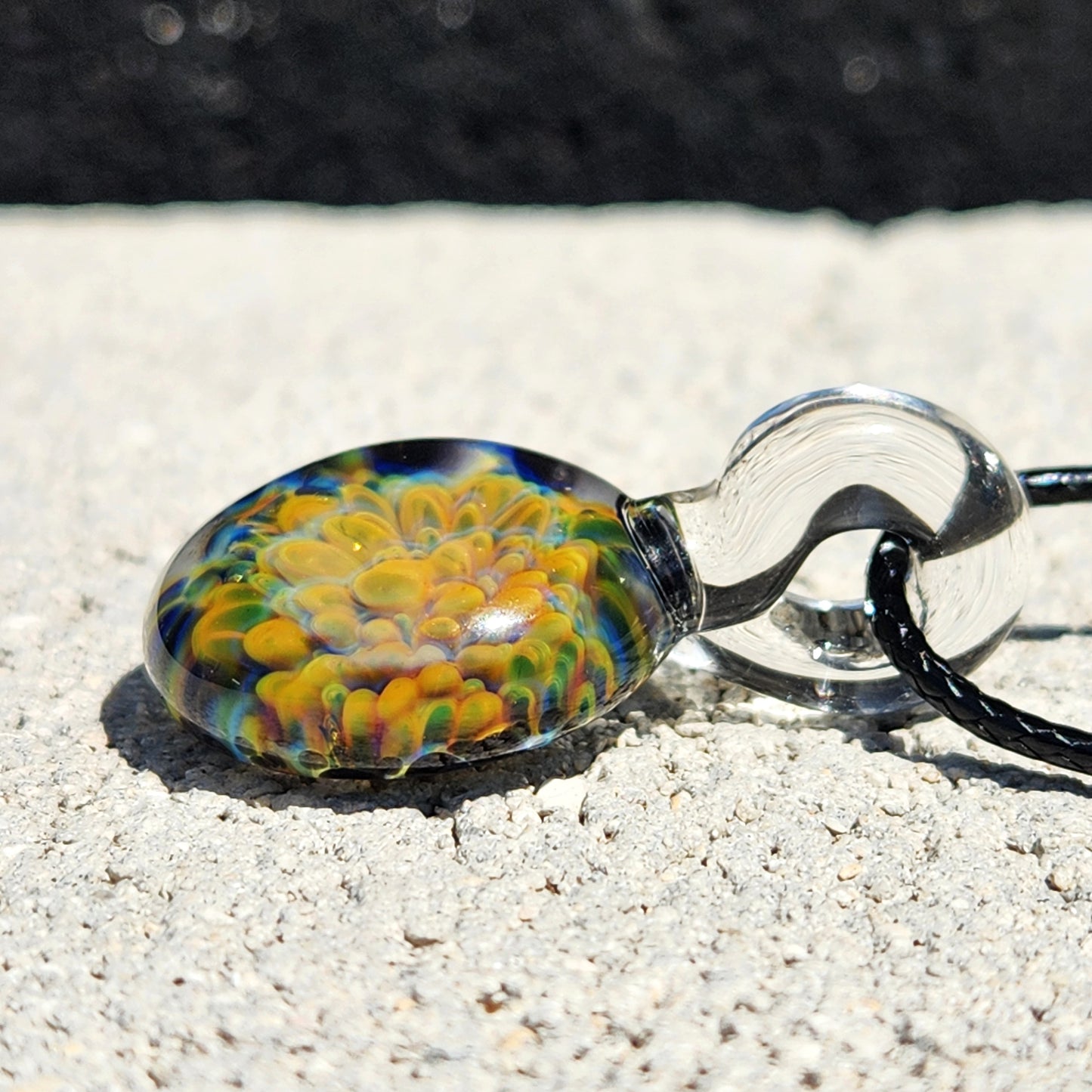 Close-up side angle of green glass pendant necklace, featuring a layered floral design in yellow, green, and blue hues.
