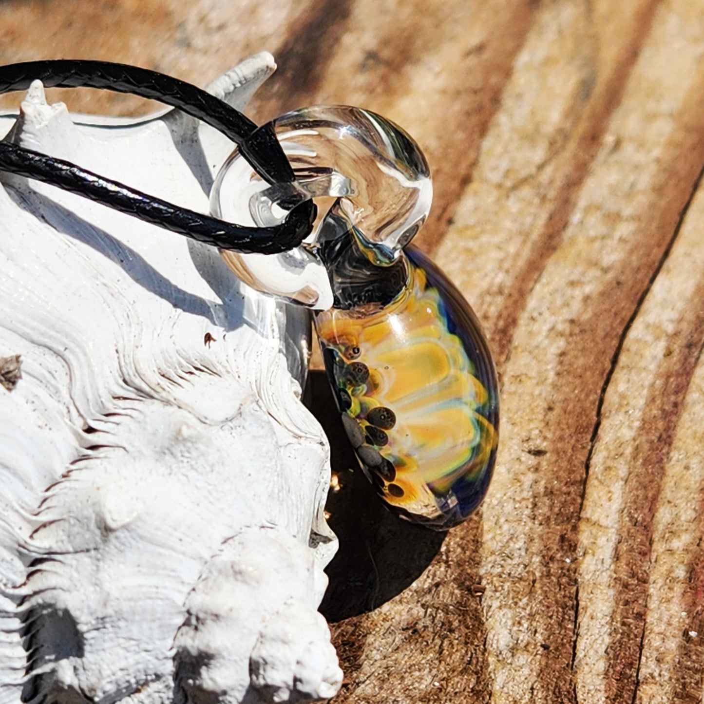 Side view of handmade blown glass pendant with colorful floral core, highlighting its transparent loop and craftsmanship.