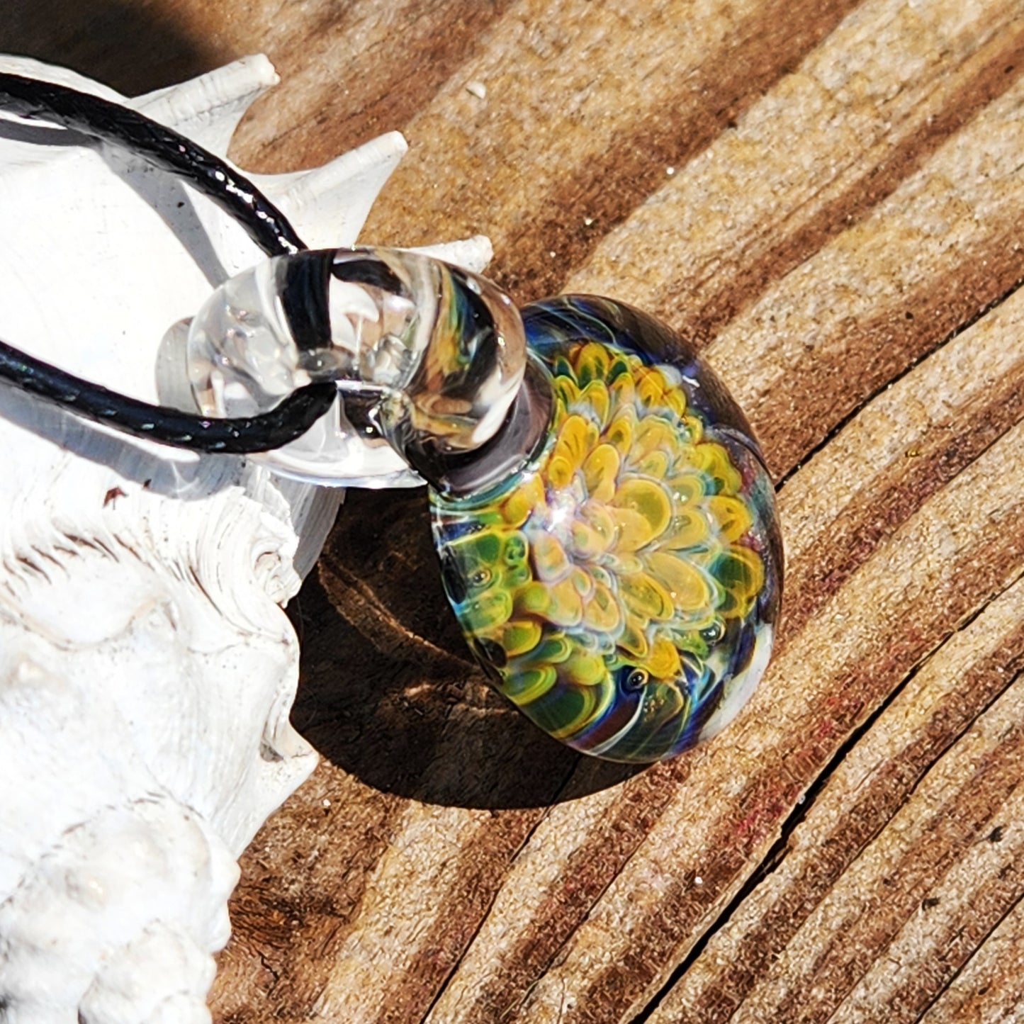 Detailed view of handmade glass pendant with swirling flower design, suspended on a black cord for a unique jewelry look.