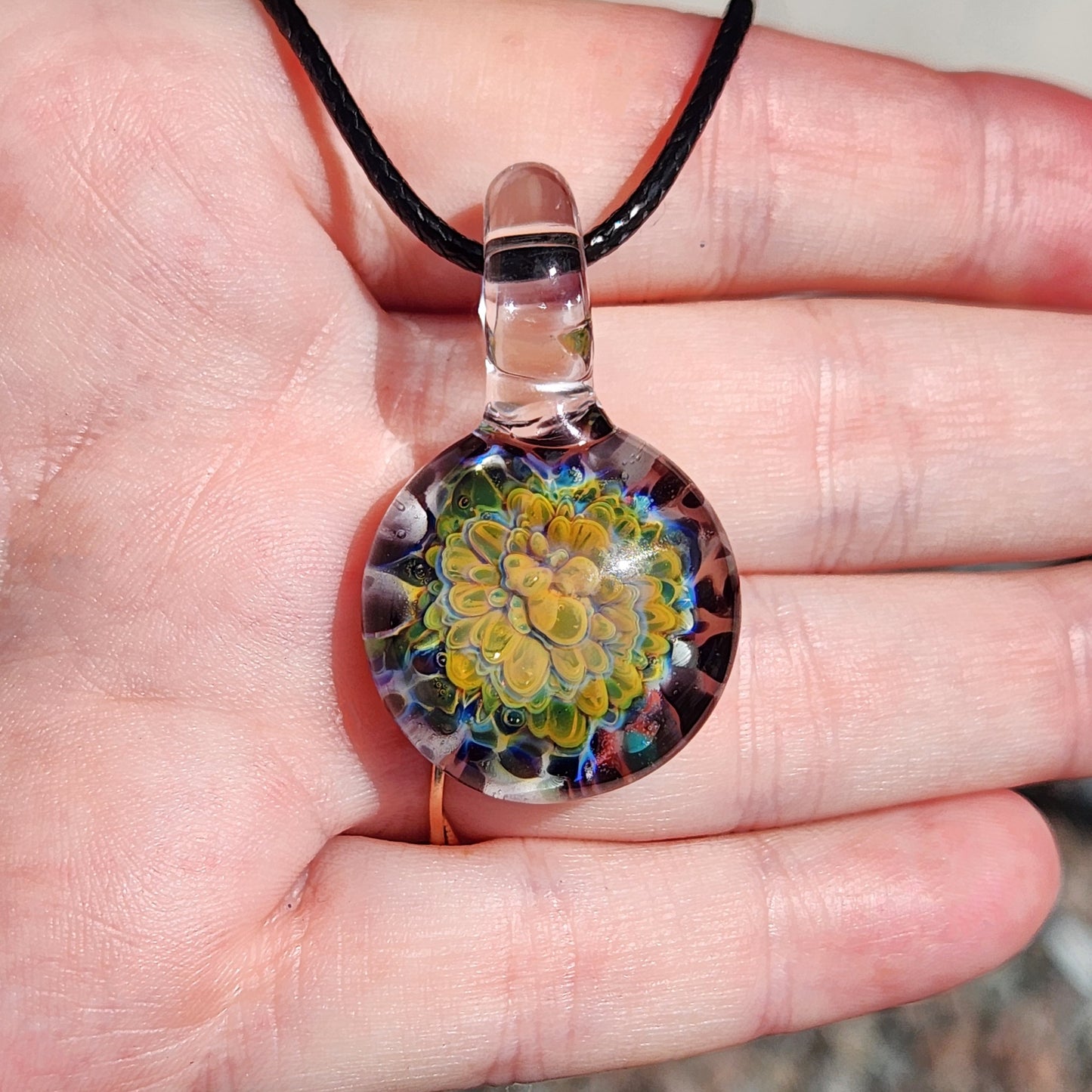 Green glass pendant necklace displayed in hand, featuring a vibrant multicolor flower design, handmade and one of a kind.