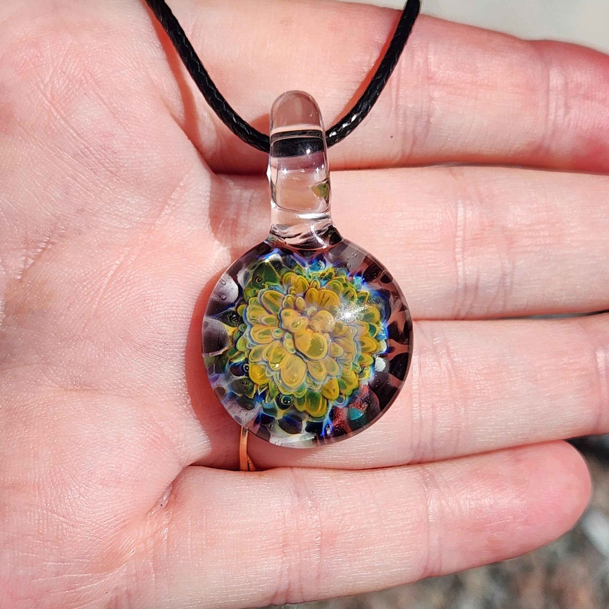 Green glass pendant necklace displayed in hand, featuring a vibrant multicolor flower design, handmade and one of a kind.