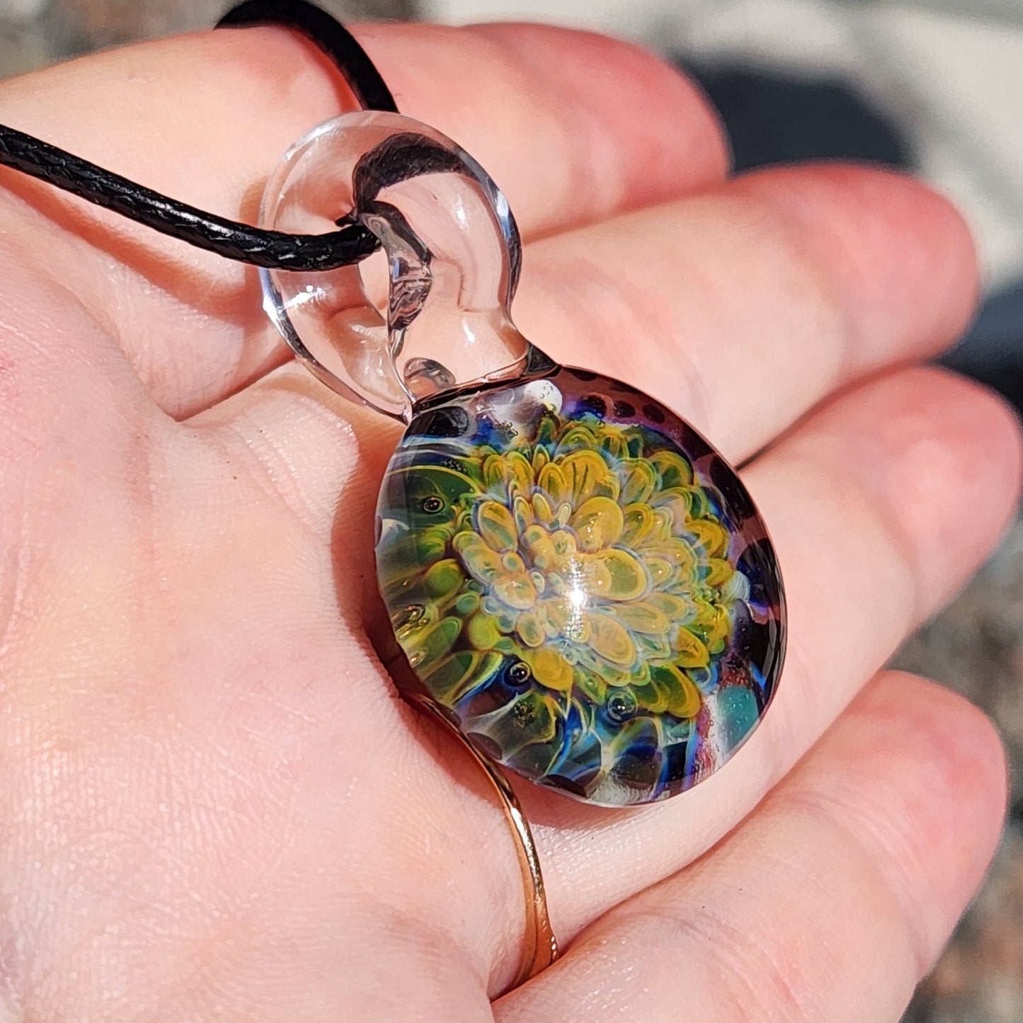 Hand holding a green glass pendant necklace with intricate yellow flower design, highlighting its handmade quality and detail.