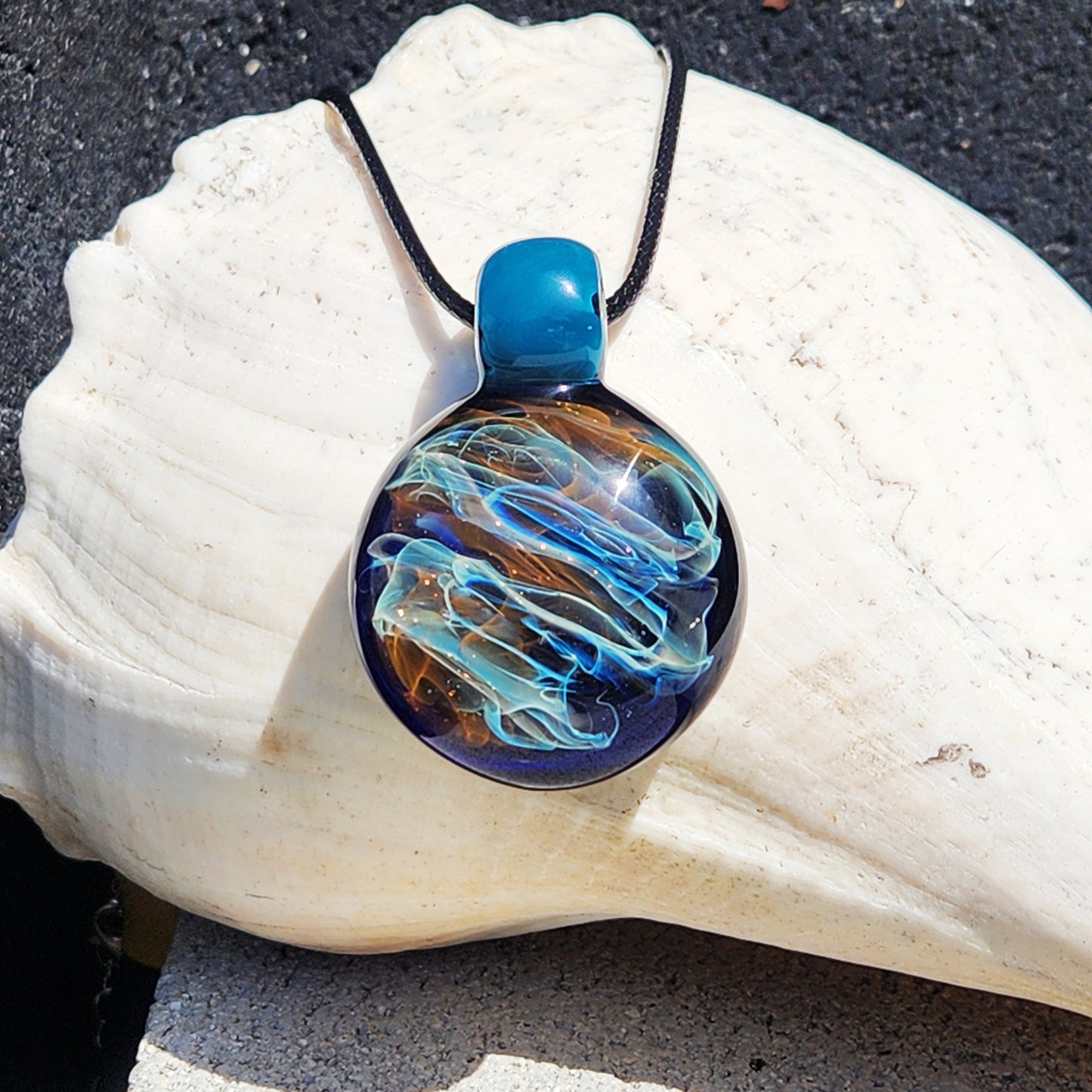 Handmade glass pendant necklace featuring vibrant gold and silver swirls in borosilicate glass. Displayed on a white seashell for jewelry gifting.