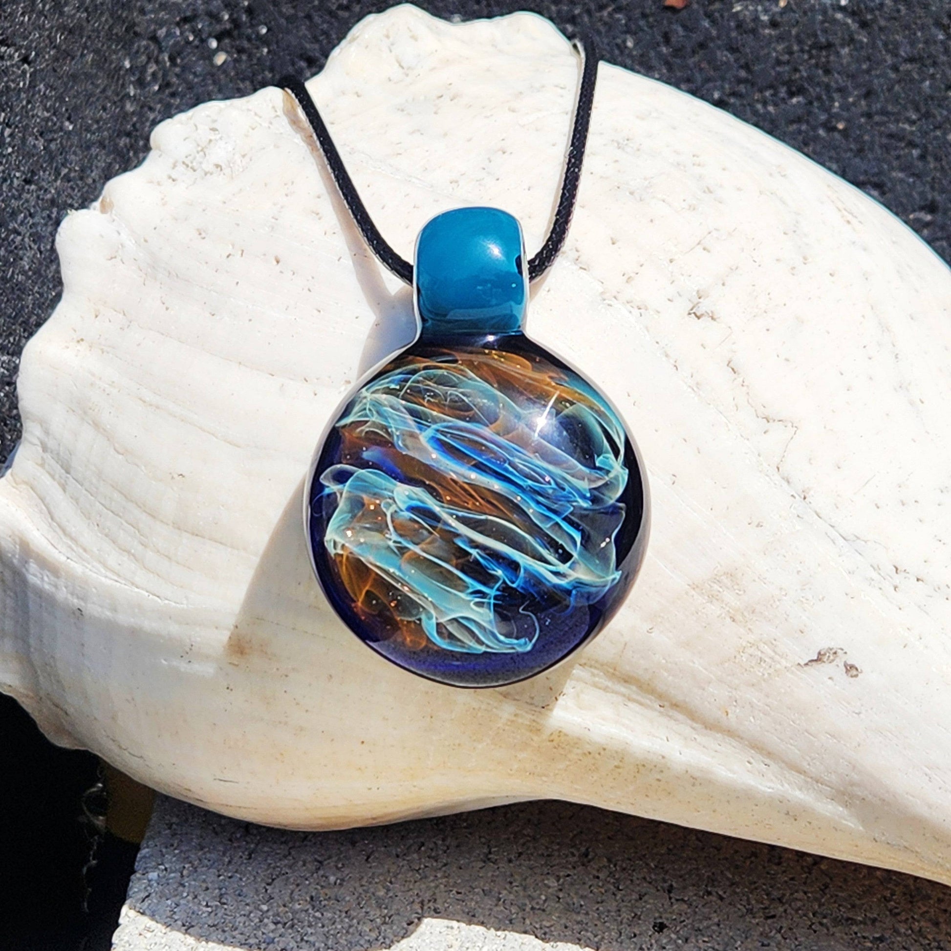 Handmade glass pendant necklace featuring vibrant gold and silver swirls in borosilicate glass. Displayed on a white seashell for jewelry gifting.