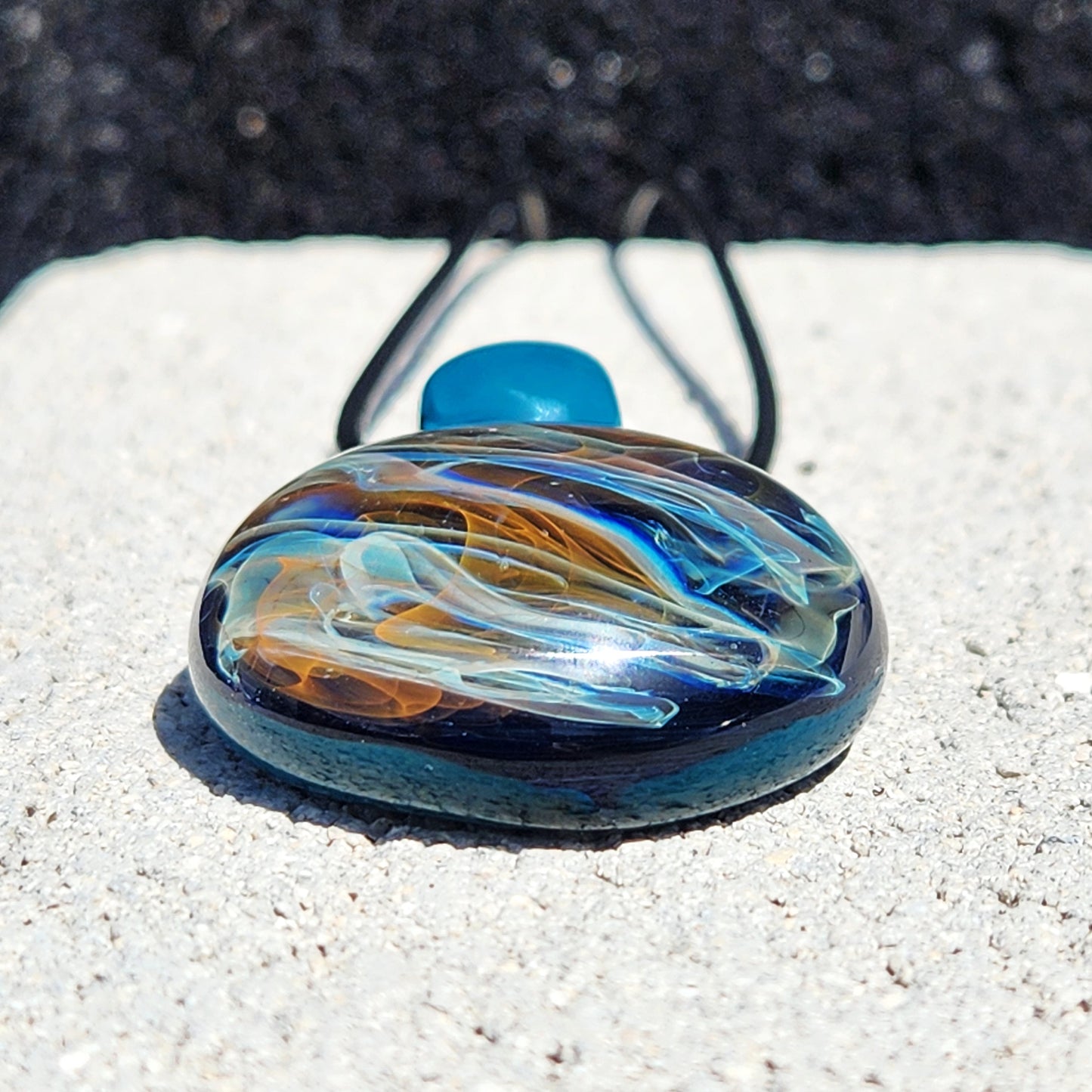 Flat view of handmade glass pendant necklace with vivid swirling colors. Borosilicate jewelry gift featuring gold and silver in a round design.