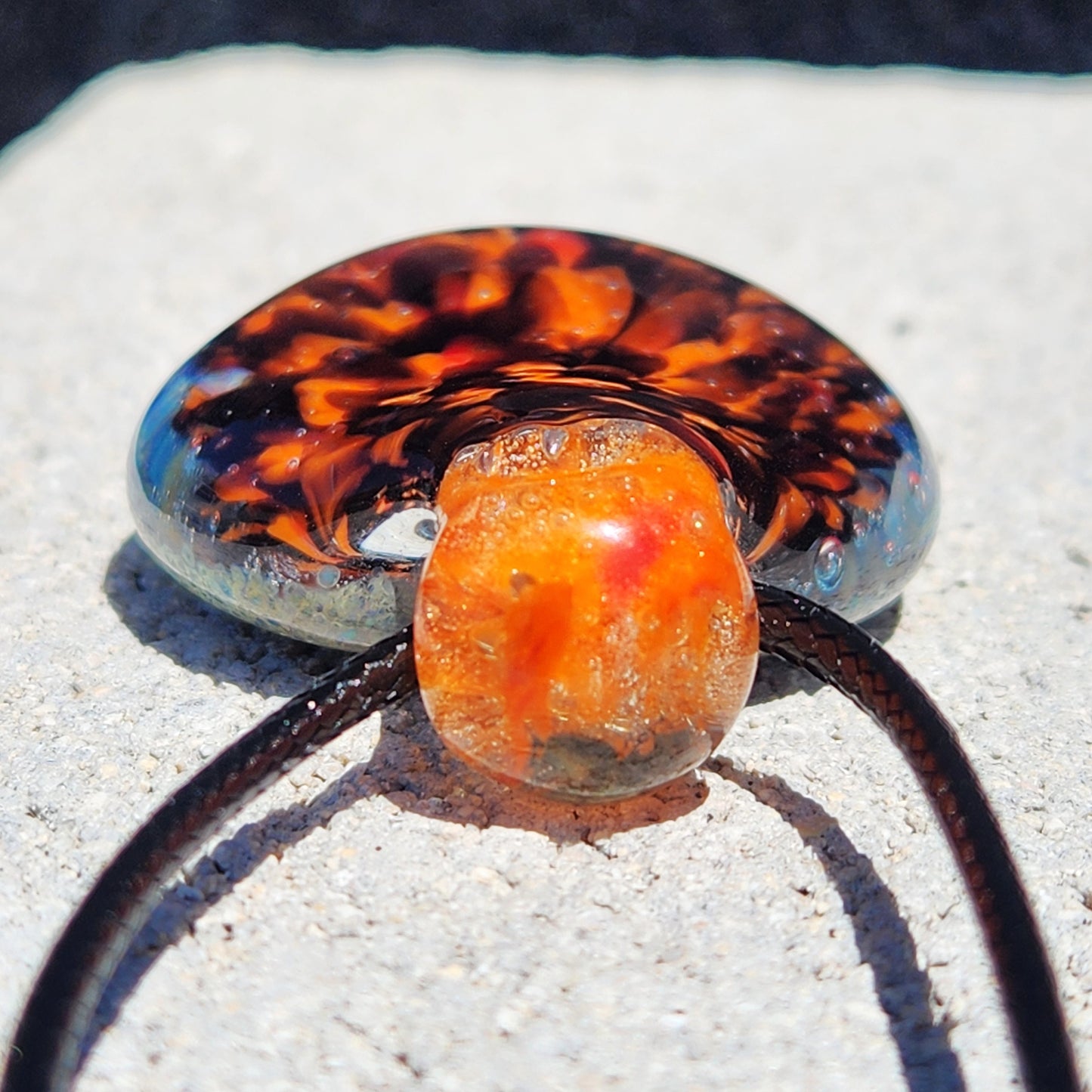 Close-up of orange and red borosilicate glass pendant top, showing detailed craftsmanship. Handmade necklace for jewelry and accessories.