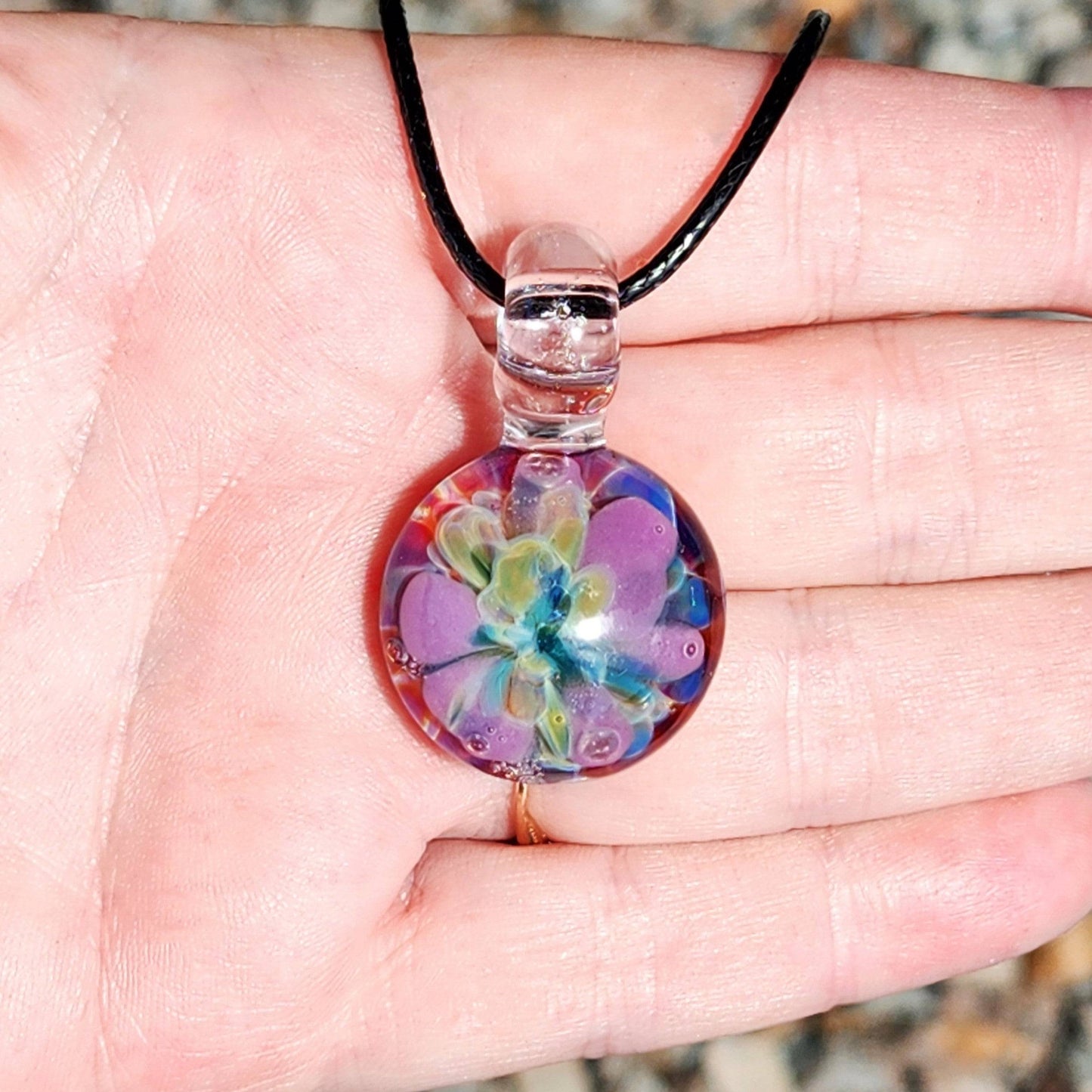Front view of small purple glass pendant necklace with multicolor flower, displayed in hand for size reference.