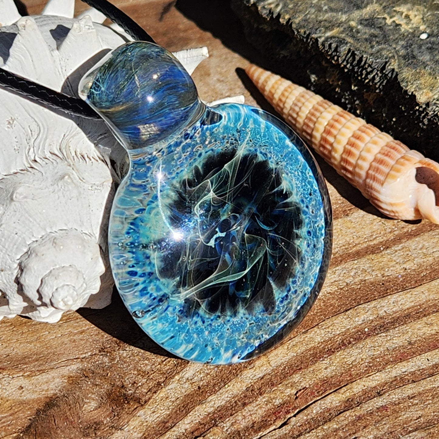 Handmade Pendant Necklace – Winter Scene Borosilicate Glass Pendant resting on wood with seashells, showcasing its oceanic design.