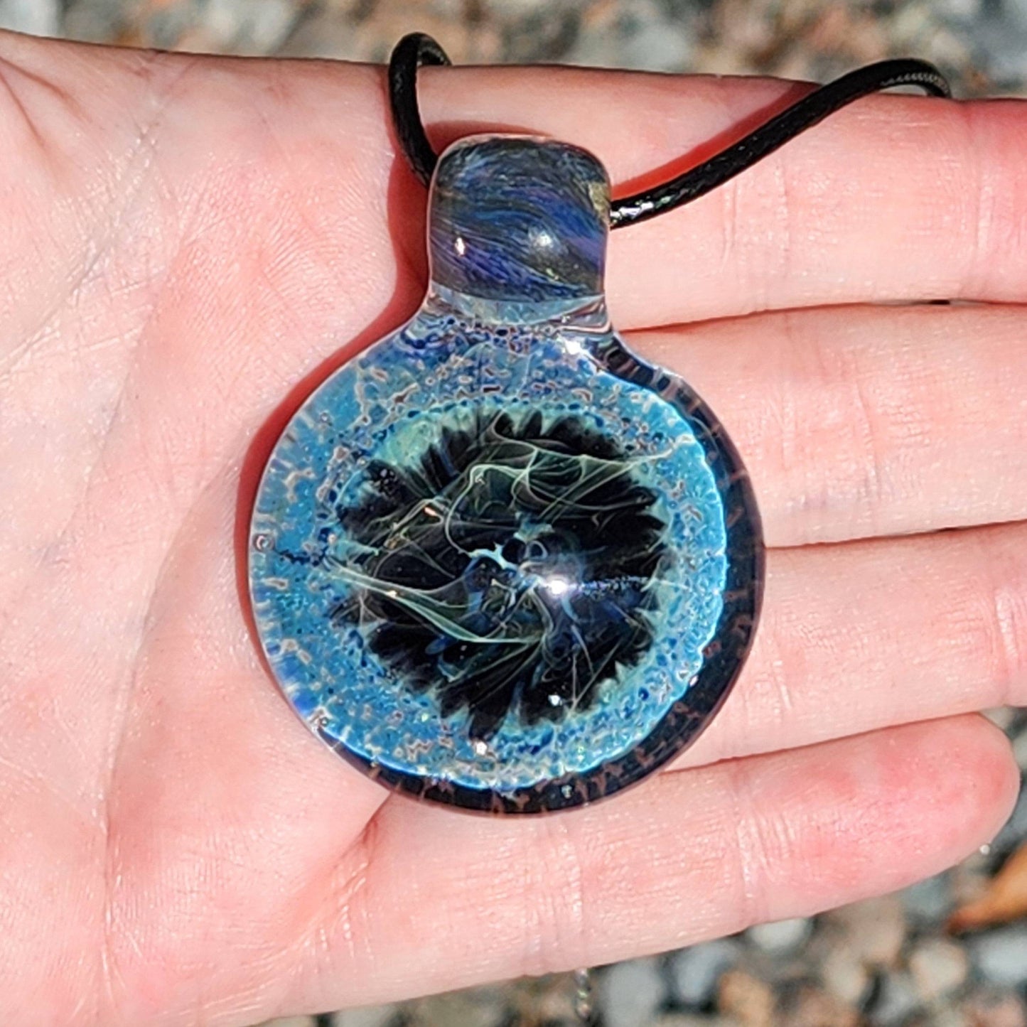Hand displaying Handmade Pendant Necklace – Winter Scene Borosilicate Glass Pendant with swirling blue and black winter scene.