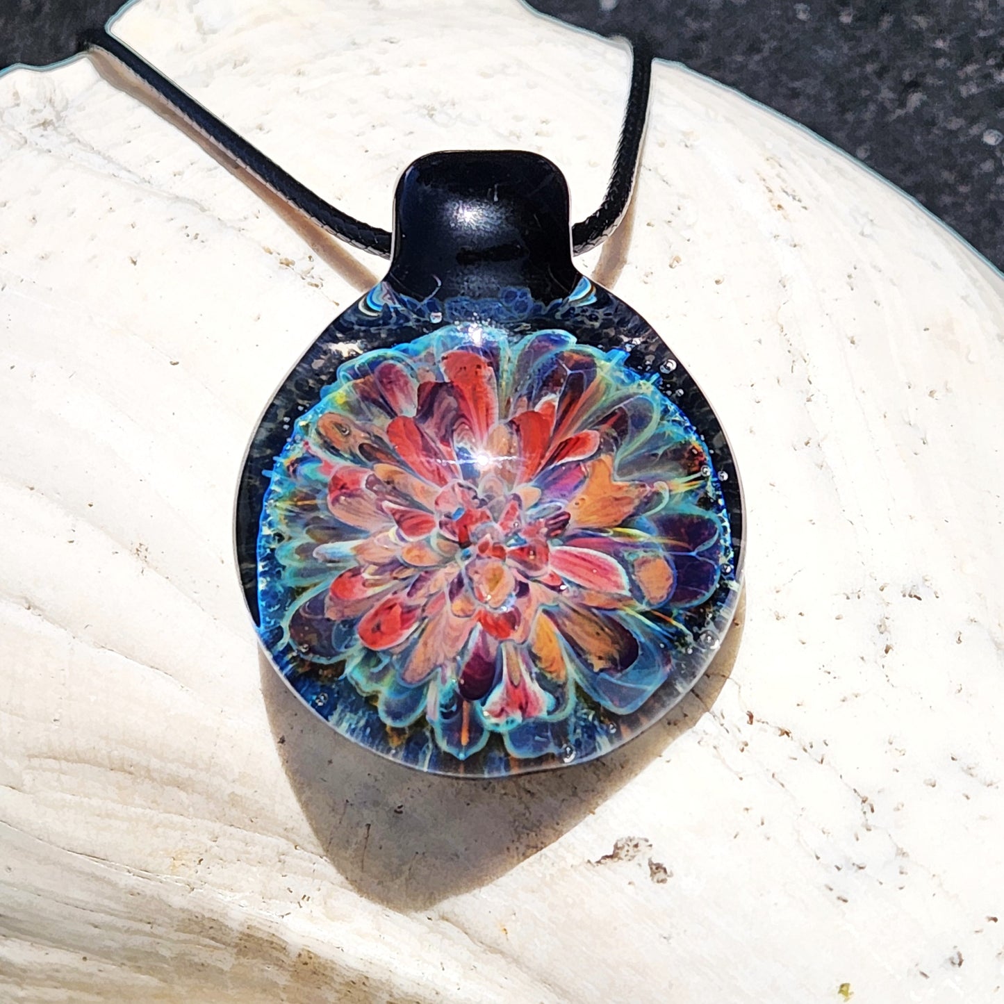 Handmade blown glass pendant necklace with vibrant red, orange, and blue floral design. Unique artisan jewelry gift in borosilicate glass.