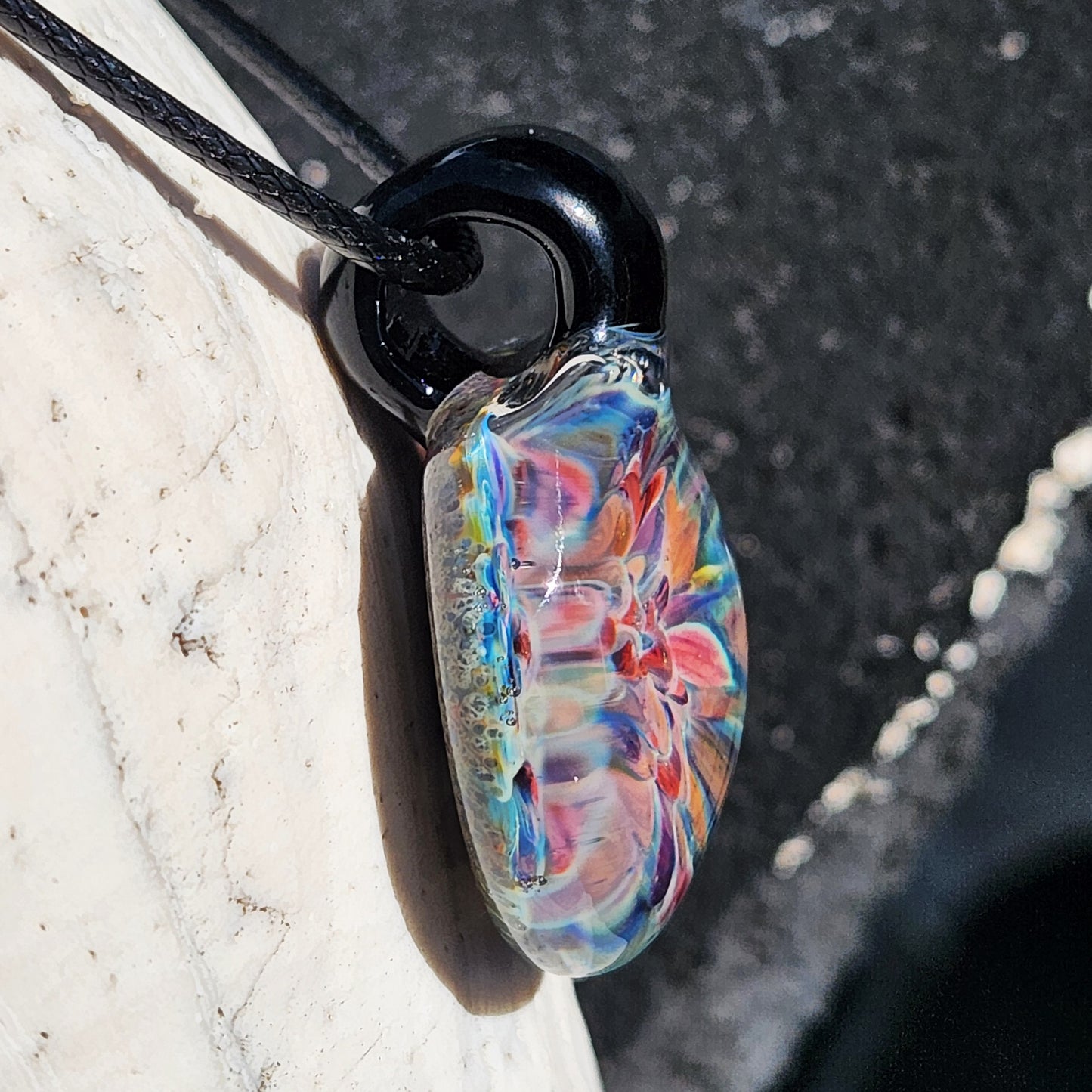Side detail of handmade blown glass pendant with looped black cord. Vibrant artisan jewelry with floral design.