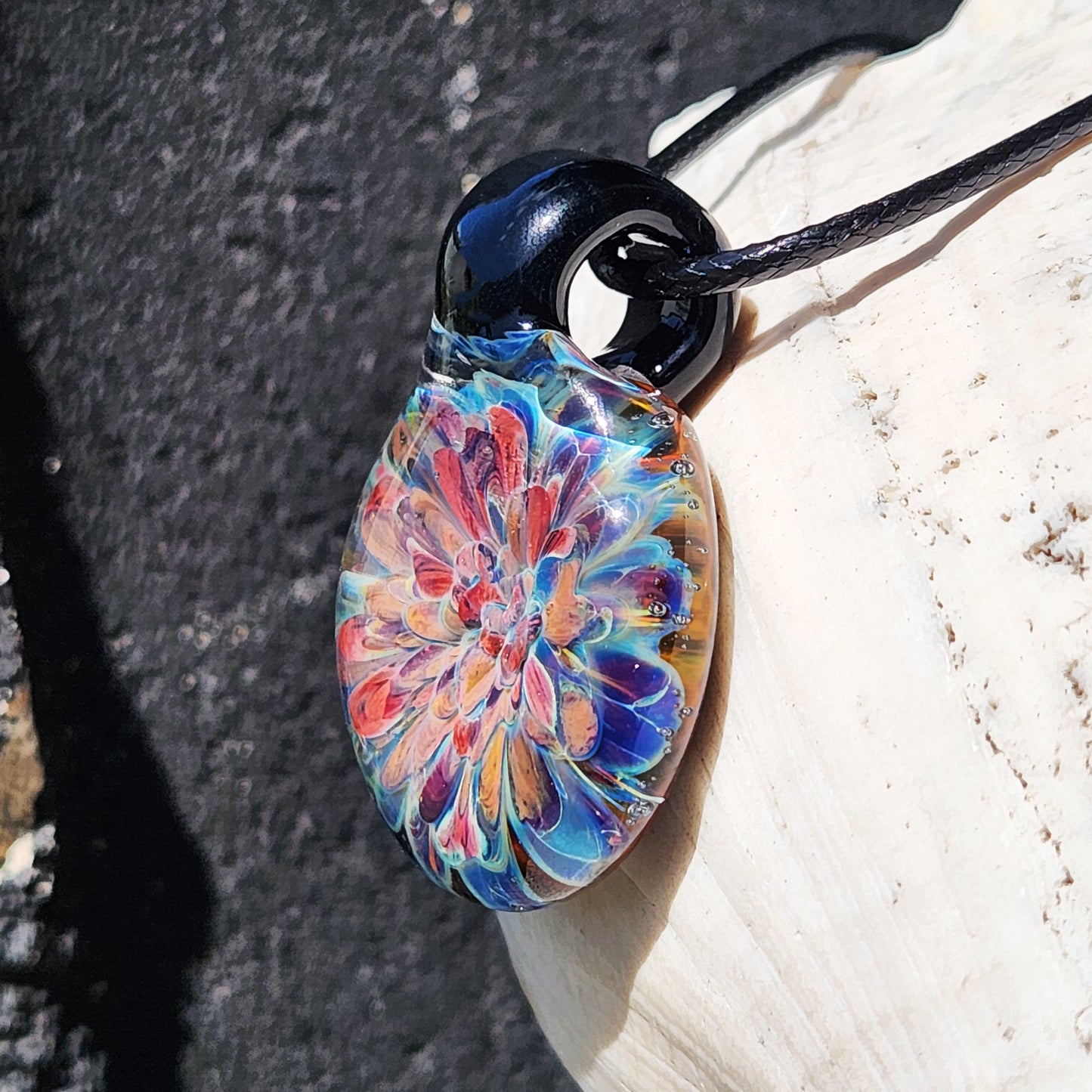 Angled close-up of artisan glass pendant showing vivid floral pattern. Handmade borosilicate jewelry gift necklace.
