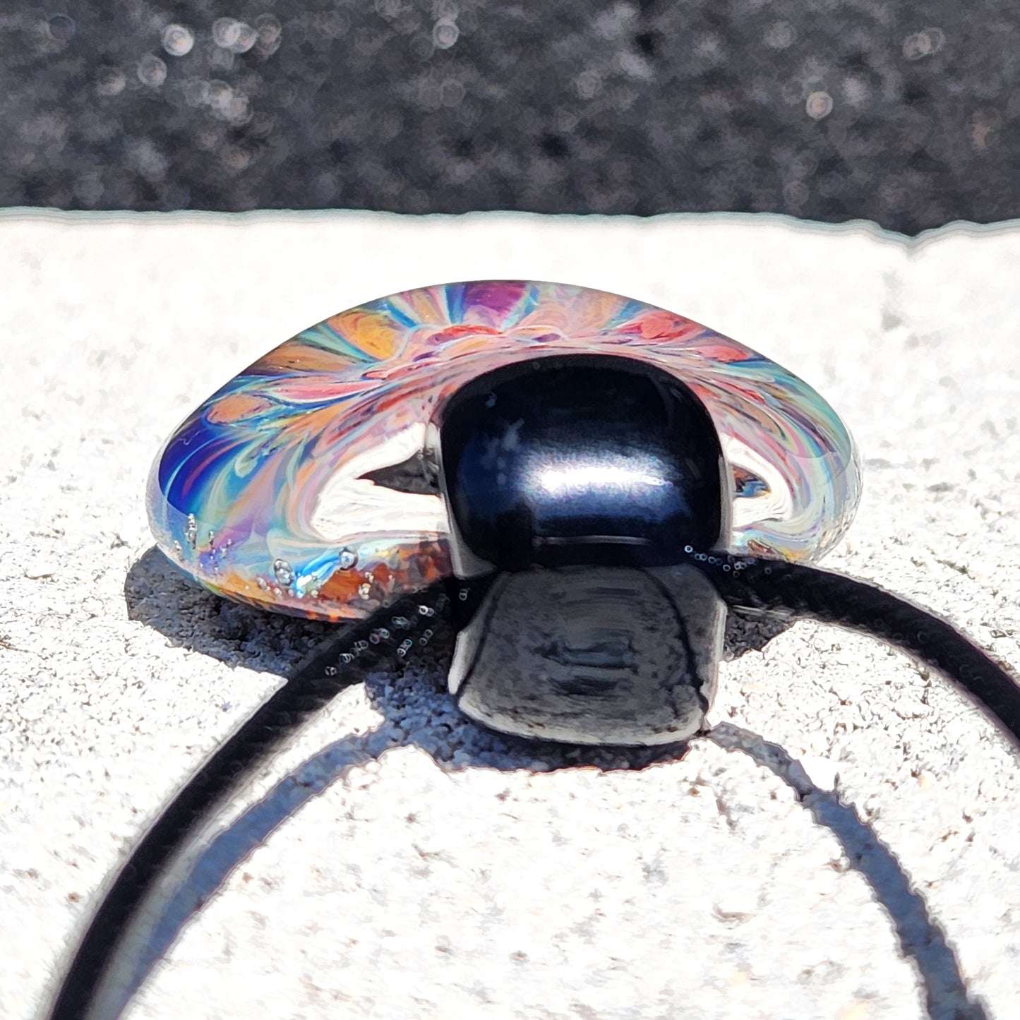 Back view of handmade glass pendant showing black loop and cord. Unique blown glass jewelry with colorful flower.