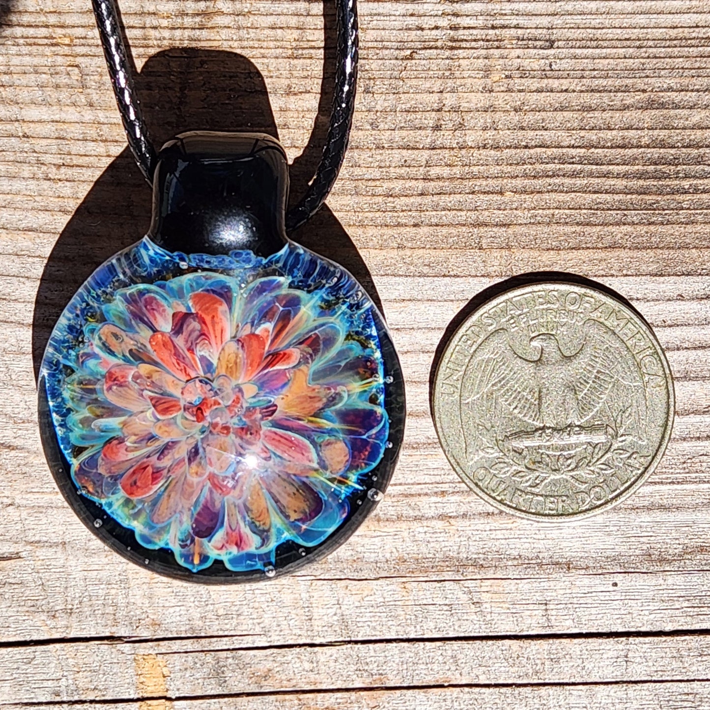 Size comparison of handmade glass pendant next to a US quarter. Artisan jewelry gift with vibrant floral design.