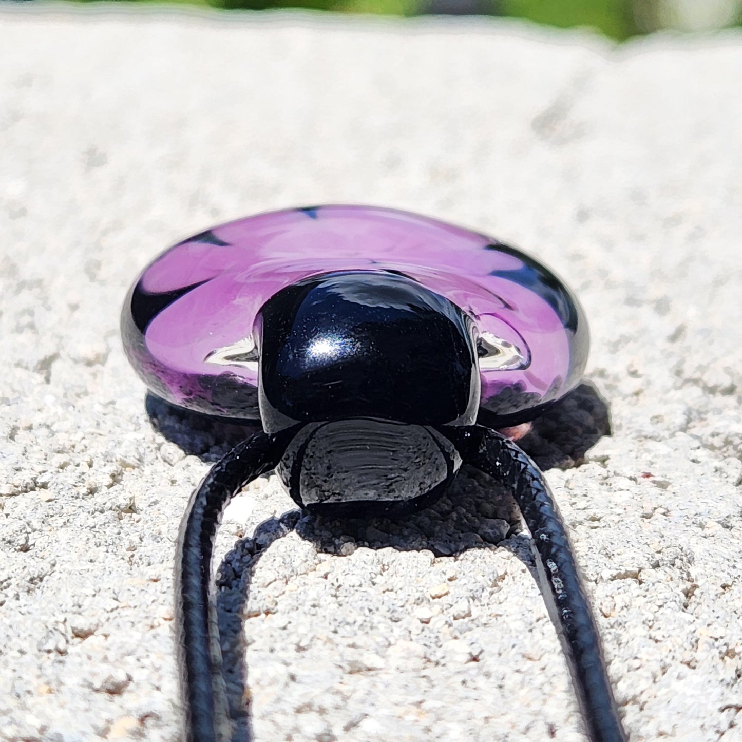 Bottom view of minimalist purple glass pendant with black base, showing cord attachment and handmade craftsmanship.