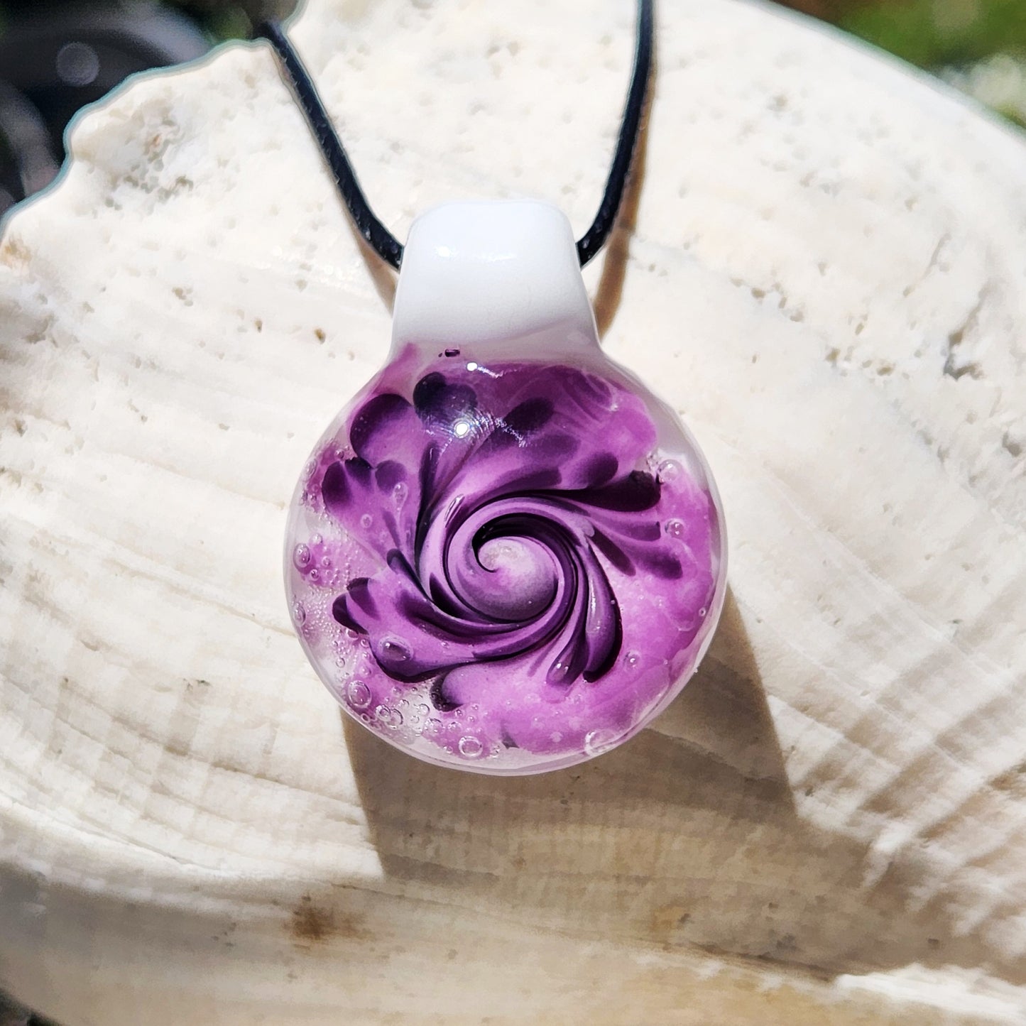 Handmade purple spiral glass pendant necklace with black swirls and white background, shown against a white seashell for contrast.