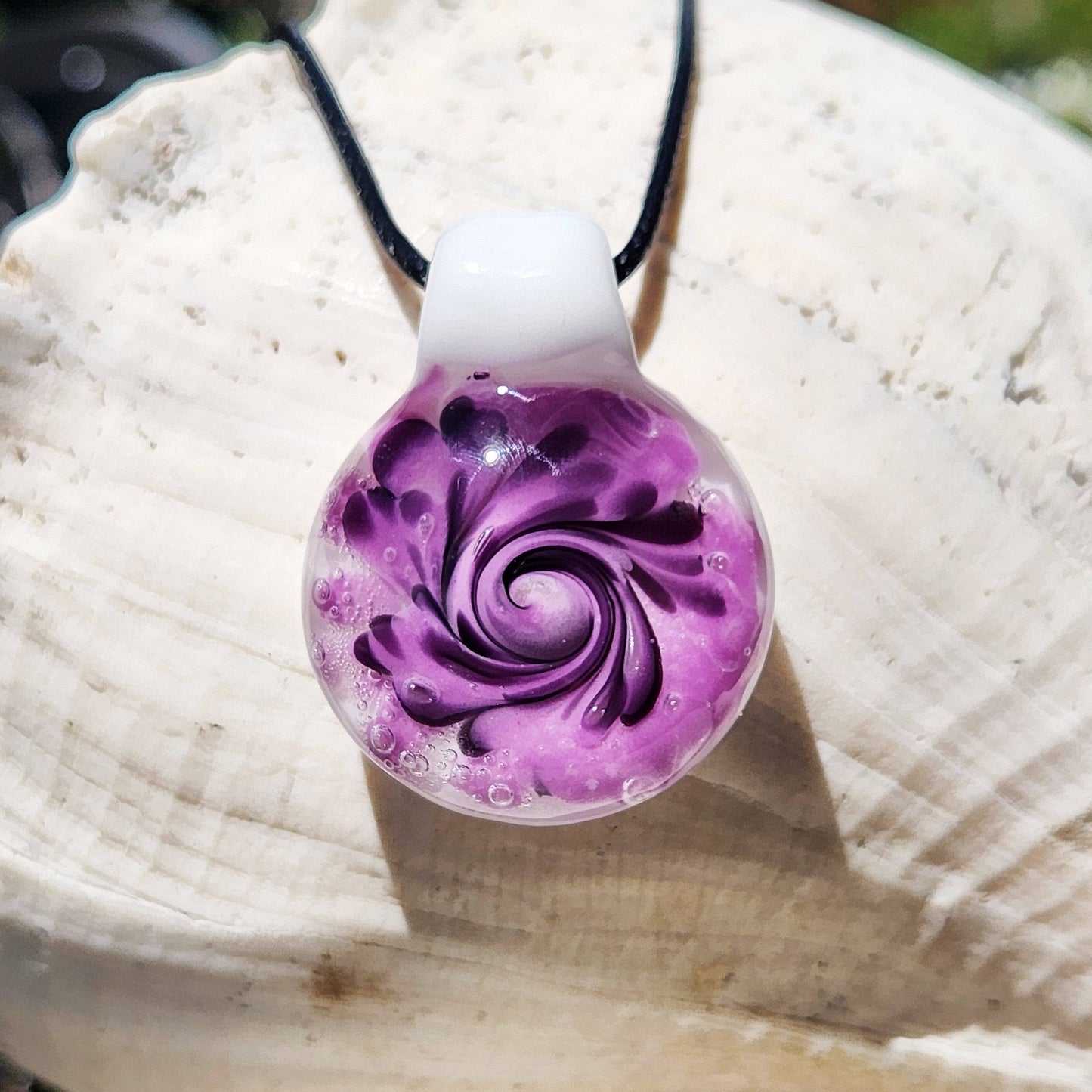 Handmade purple spiral glass pendant necklace with black swirls and white background, shown against a white seashell for contrast.