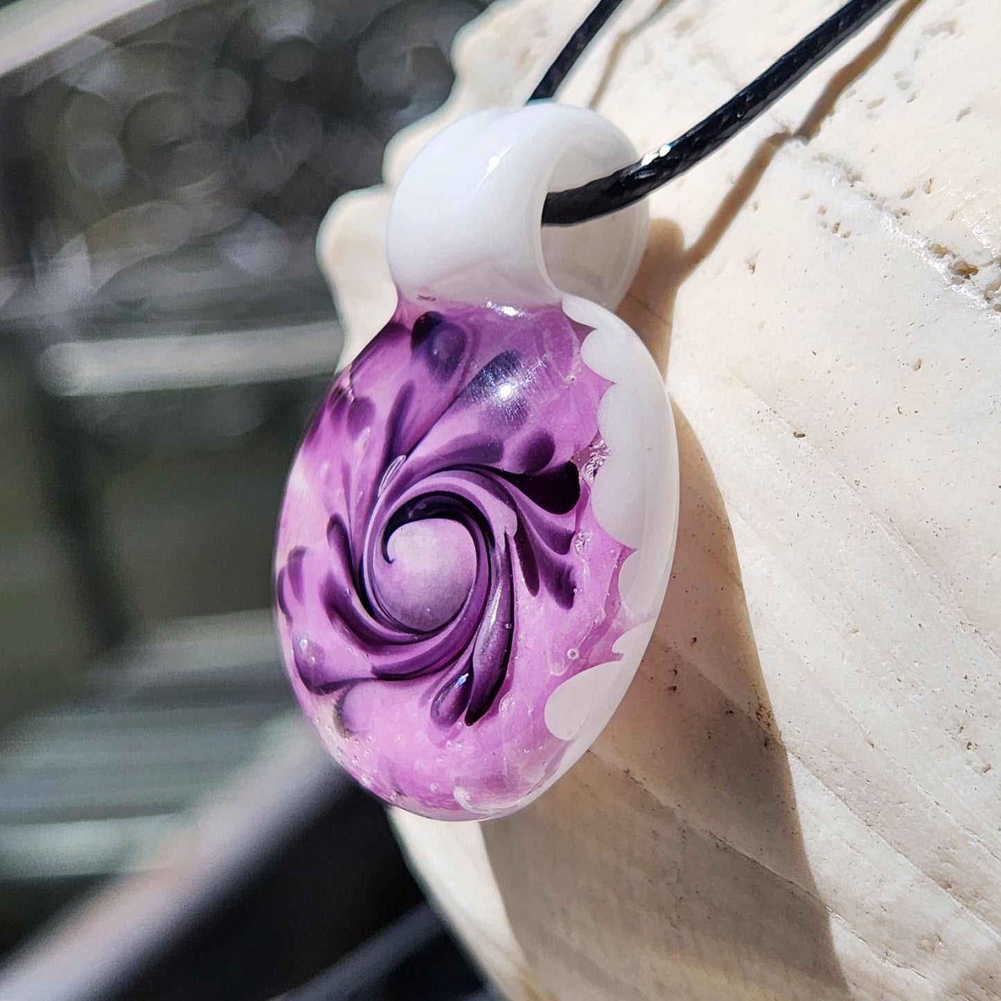 Purple spiral handmade glass pendant necklace with white top loop, displayed hanging against a seashell background.