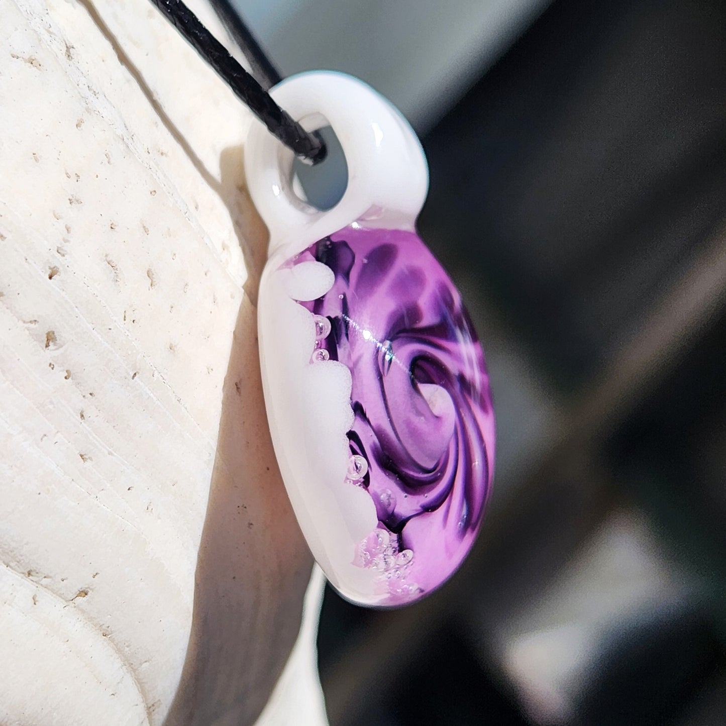 Side view of handmade purple spiral glass pendant necklace with white and black swirl design, hanging on a black cord.