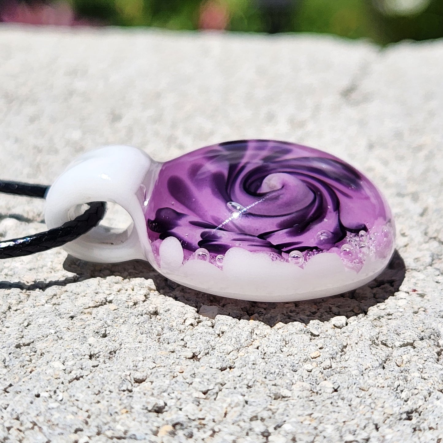 Purple spiral glass pendant necklace with white and black accents, handmade and resting on a textured stone surface.