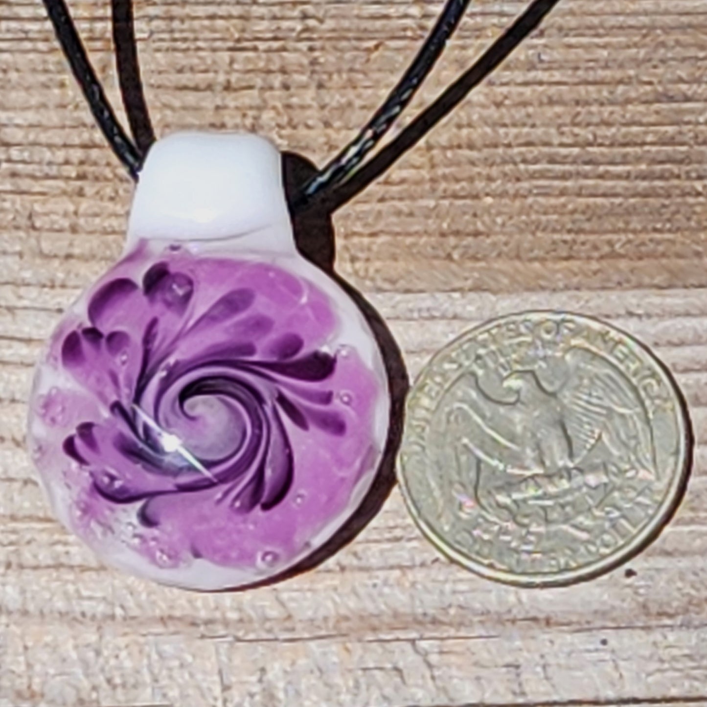 Purple spiral handmade glass pendant necklace shown next to a U.S. quarter for size comparison, highlighting its compact design.