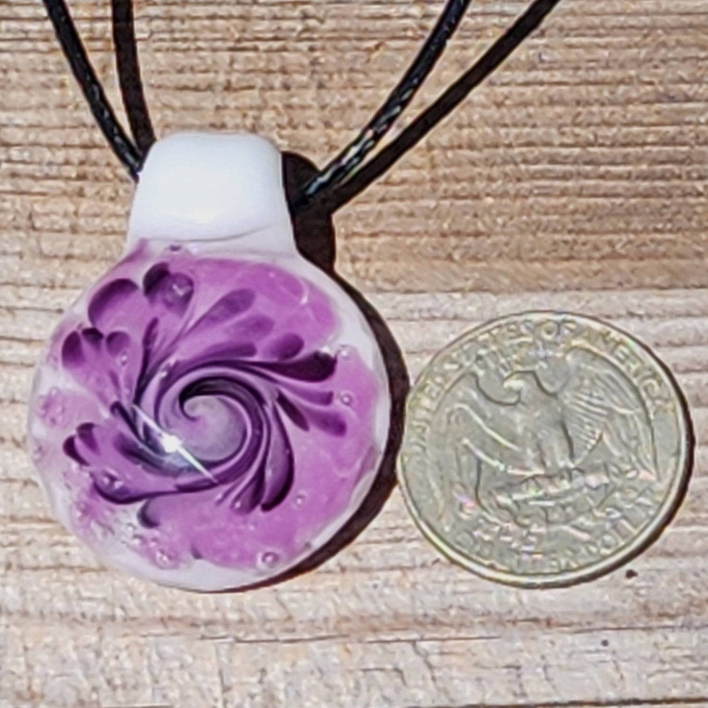 Purple spiral handmade glass pendant necklace shown next to a U.S. quarter for size comparison, highlighting its compact design.