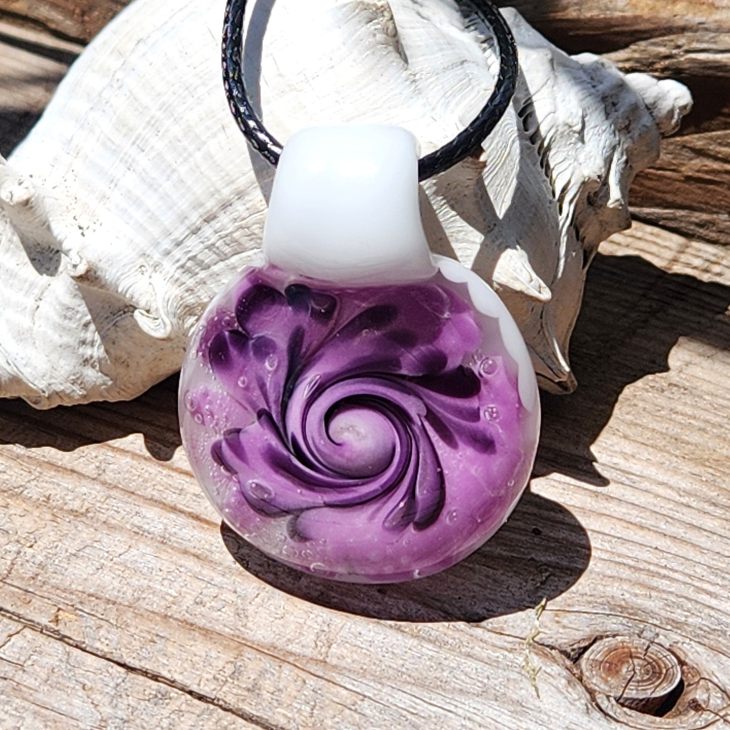 Handmade purple spiral glass pendant necklace with white base, displayed on wood with a seashell for natural contrast.