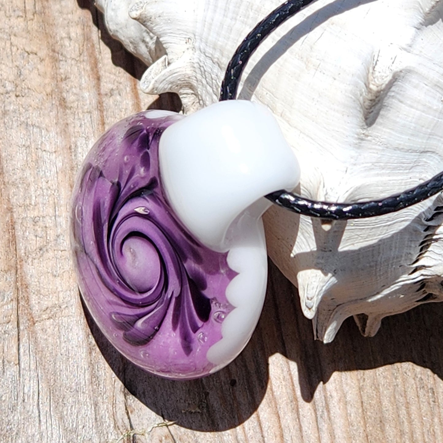 Angled view of purple spiral handmade glass pendant necklace with white top and black swirls, lying on a wooden surface.