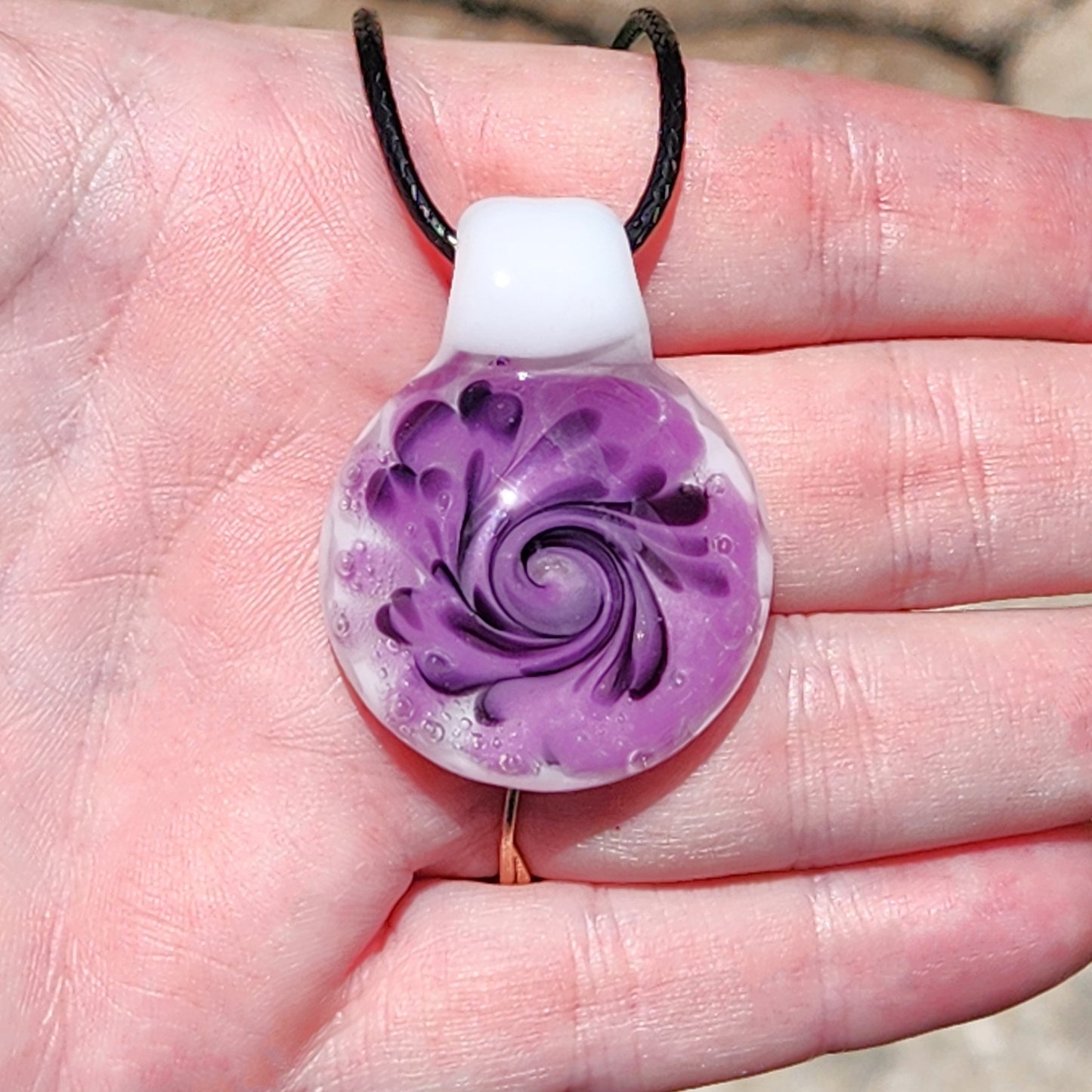 Hand holding a handmade purple spiral glass pendant necklace with white and black detailing, showcasing its size and craftsmanship.