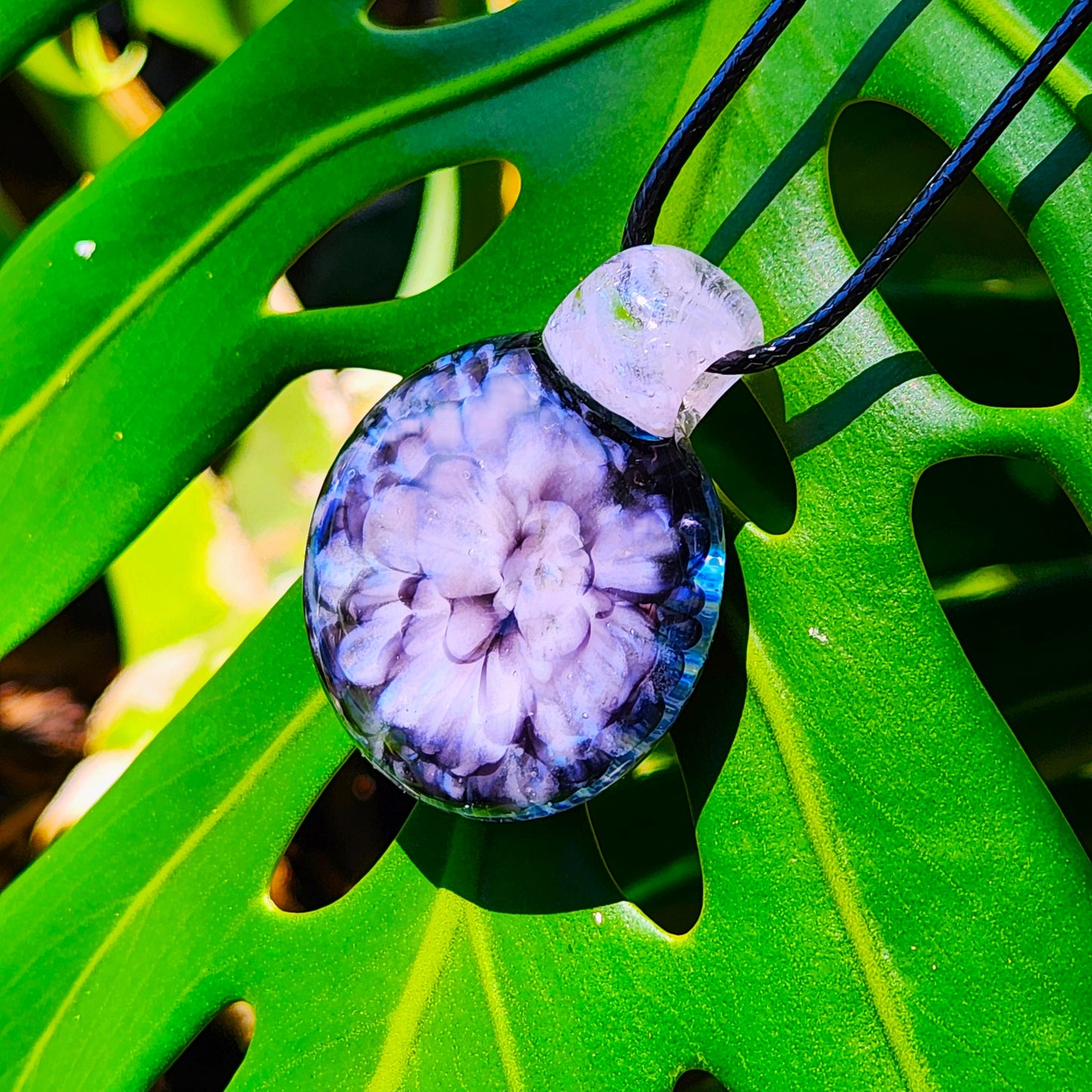 Pink crushed glass flower pendant necklace displayed on a green monstera leaf, highlighting its floral design and craftsmanship.