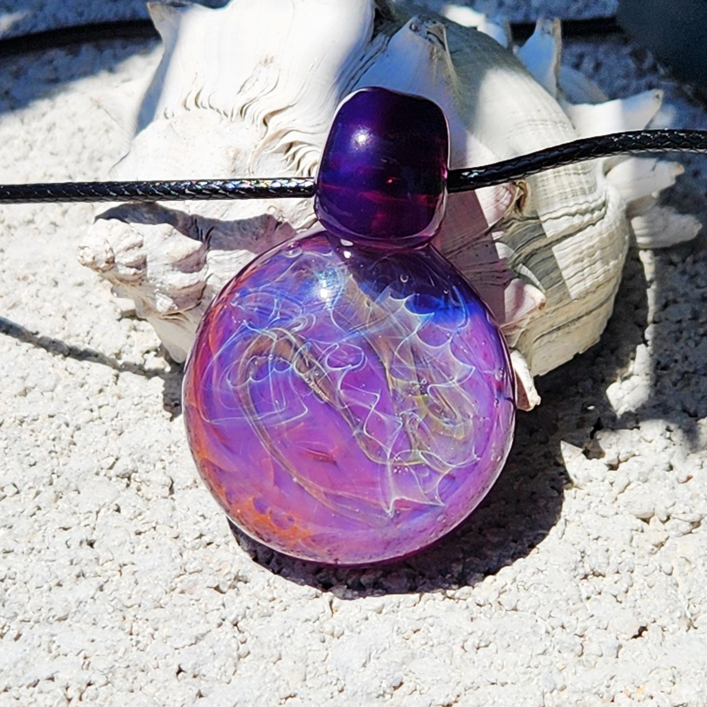 Handmade purple glass pendant with silver and gold fuming, shown on sand with seashells. Unique statement necklace for jewelry lovers.