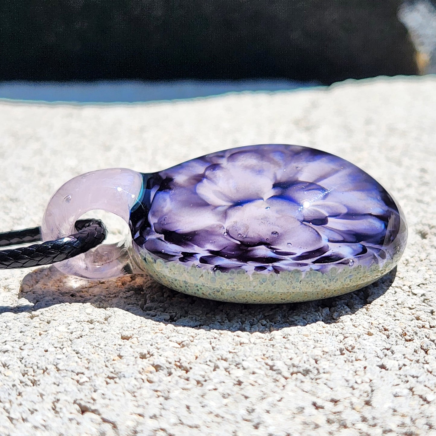 Side angle of handmade pink flower pendant necklace resting on a light stone surface, showcasing its domed glass shape.