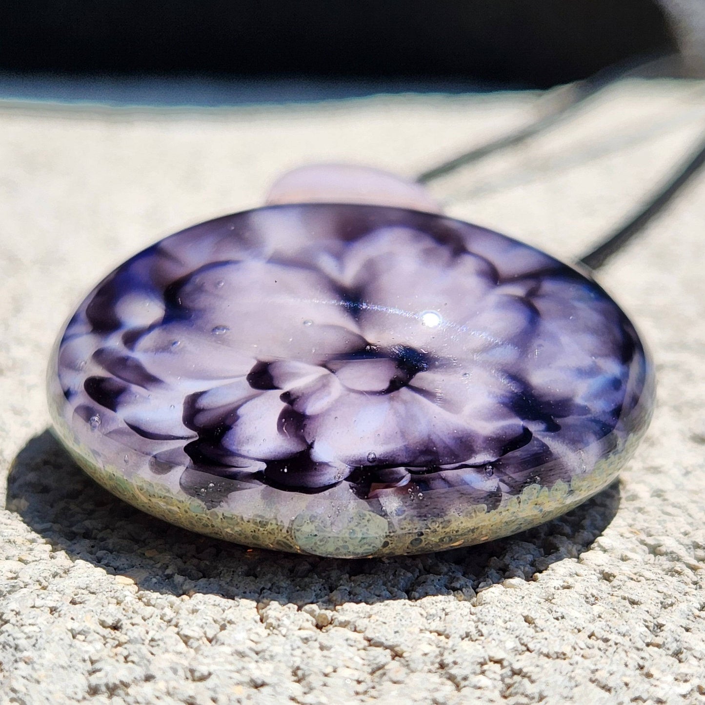 Close-up of handmade pink flower pendant necklace showing intricate glass petal details and glossy finish on a textured surface.
