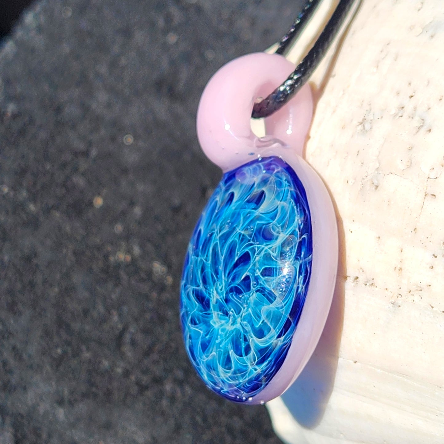 Artisan glass pendant necklace with swirling blue core and pink loop, shown in natural light. Elegant handmade jewelry gift for her.