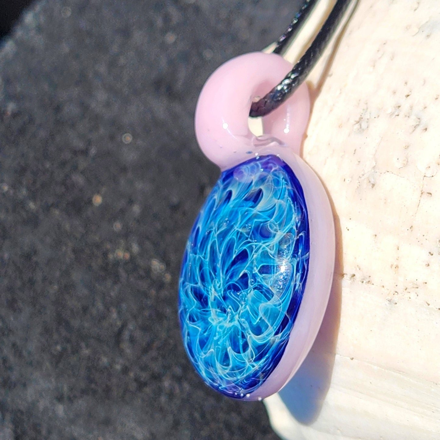 Artisan glass pendant necklace with swirling blue core and pink loop, shown in natural light. Elegant handmade jewelry gift for her.