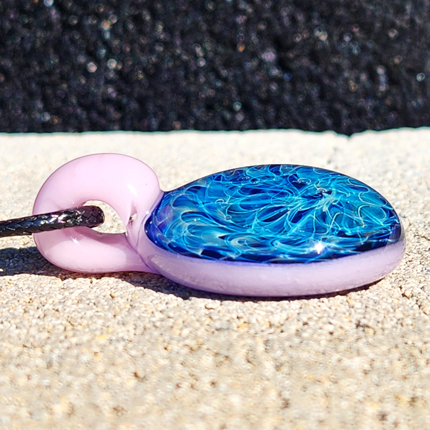 Close-up of handmade glass pendant necklace with pink loop and blue fumed design. Unique accessory in jewelry and pendants category.