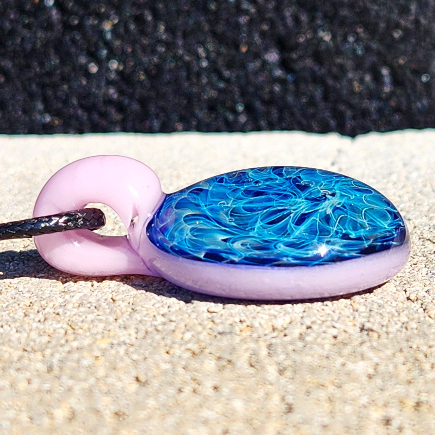 Close-up of handmade glass pendant necklace with pink loop and blue fumed design. Unique accessory in jewelry and pendants category.