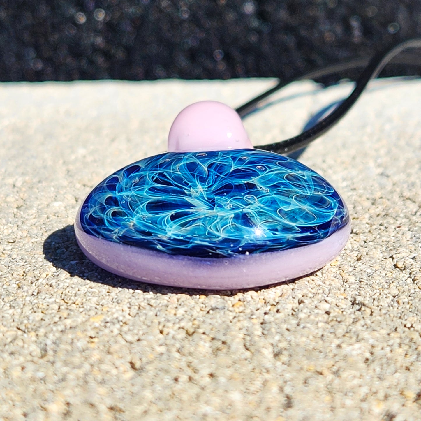 Flat view of handmade glass pendant necklace with pink loop and vibrant blue design. Unique jewelry piece in charms and pendants category.