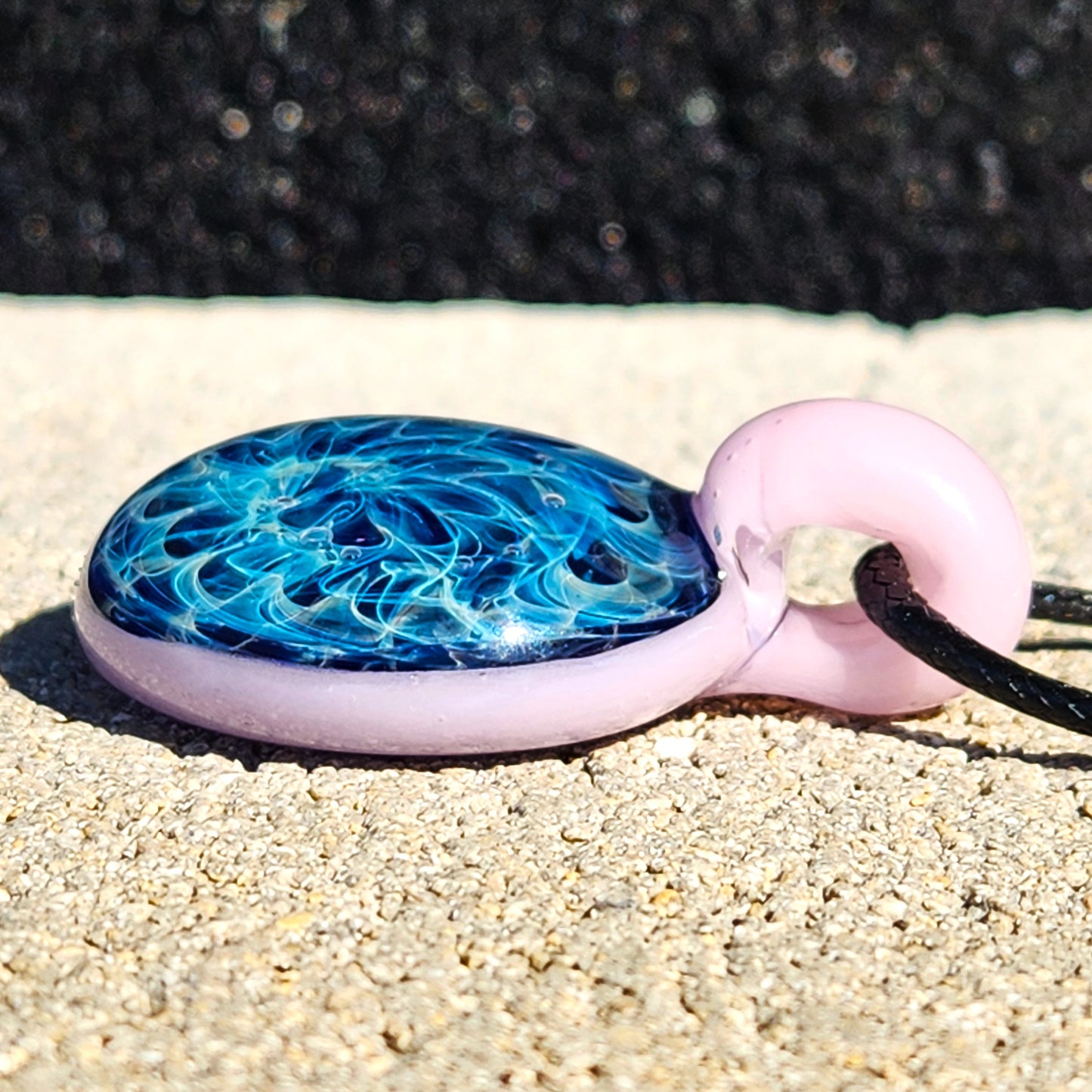 Side view of small heady glass pendant necklace showing depth of blue swirls and pink loop. Artisan-crafted jewelry with silver fuming.