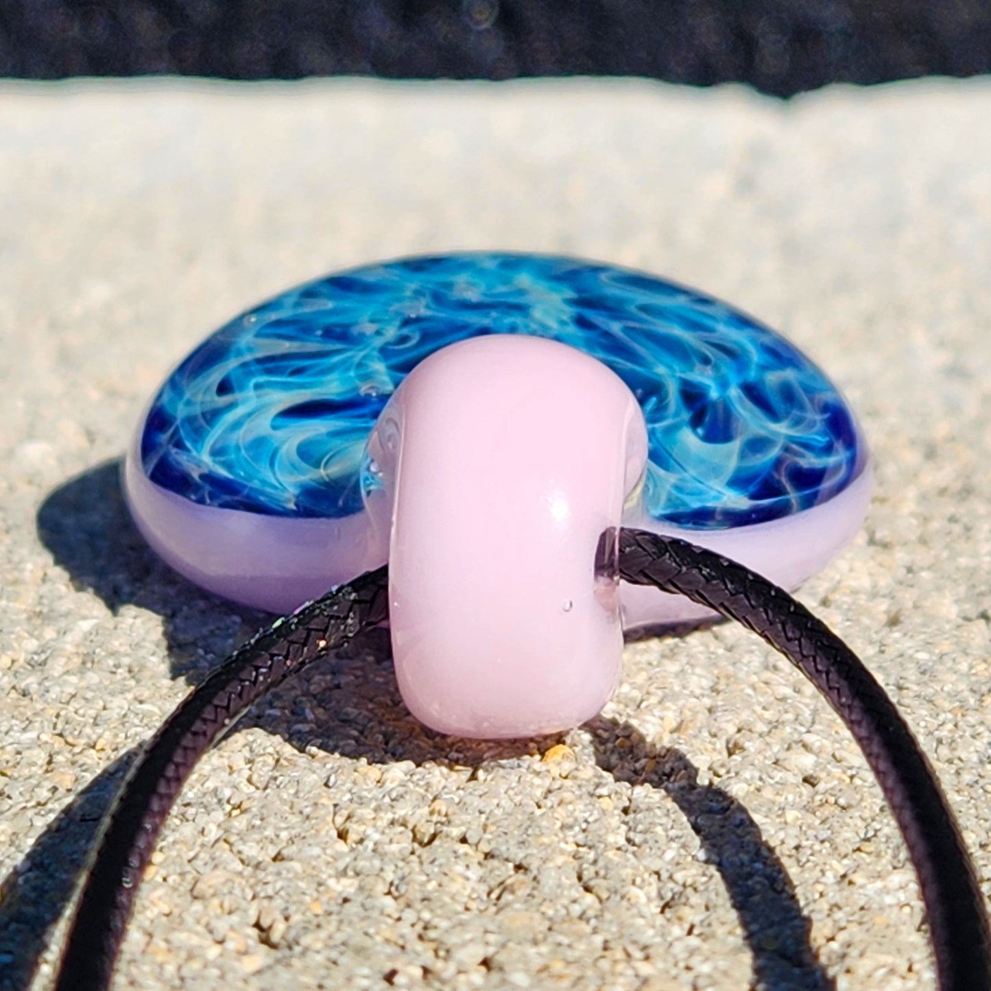 Detailed view of pink loop on heady glass pendant necklace with blue swirls. Handmade jewelry with elegant blown glass craftsmanship.