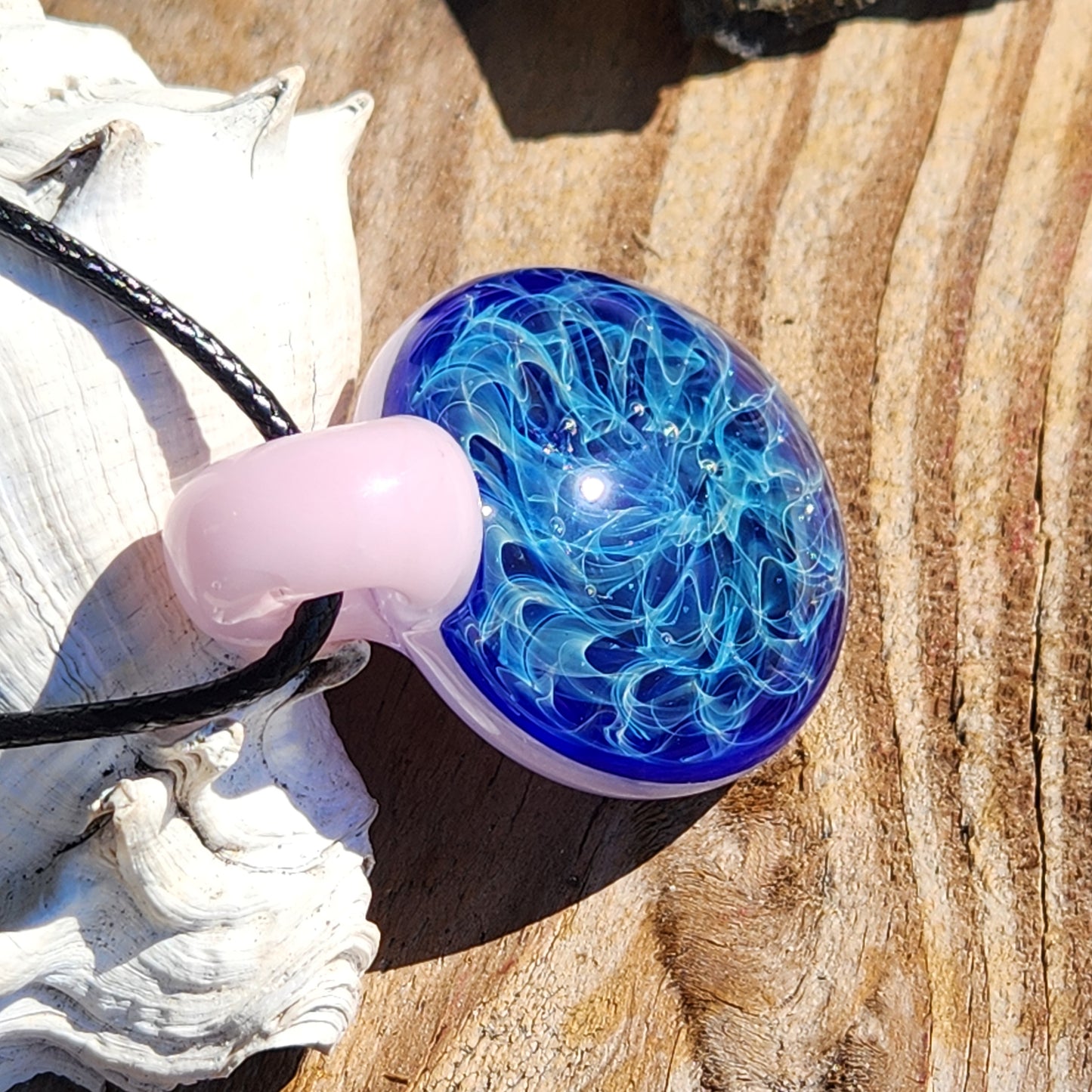 Heady glass pendant necklace with blue and white swirls, pink loop, and black cord. Blown glass charm with silver fuming.
