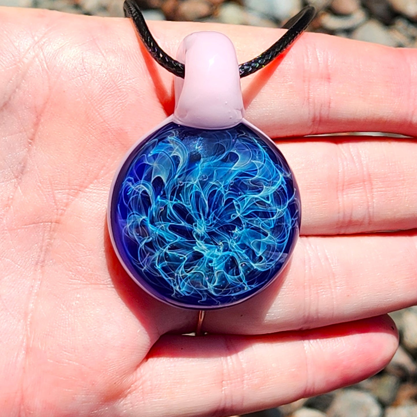 Hand holding small heady glass pendant necklace with pink loop and swirling blue design. Unique handmade jewelry gift for women.