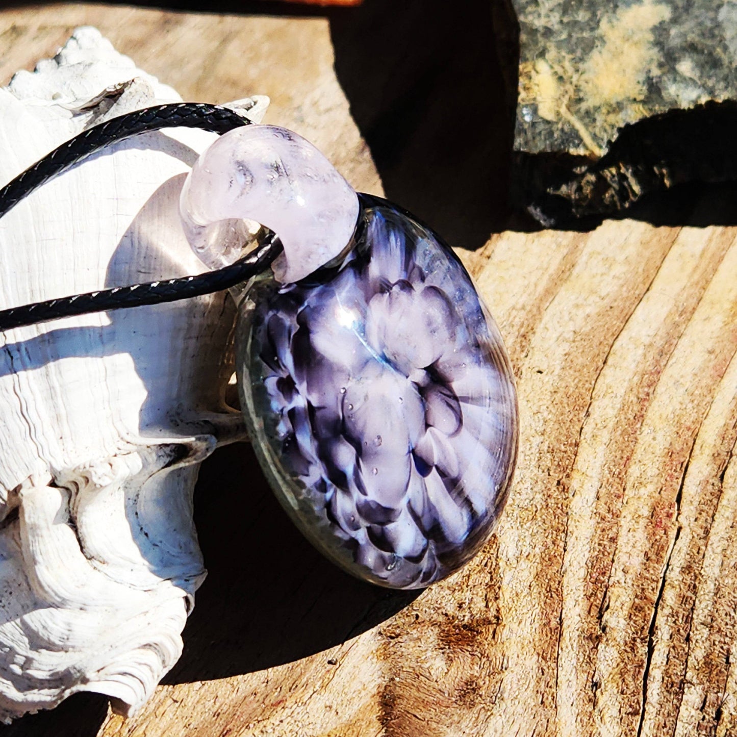 Handmade pink flower pendant necklace with crushed glass detail, photographed on wood with natural sunlight reflections.