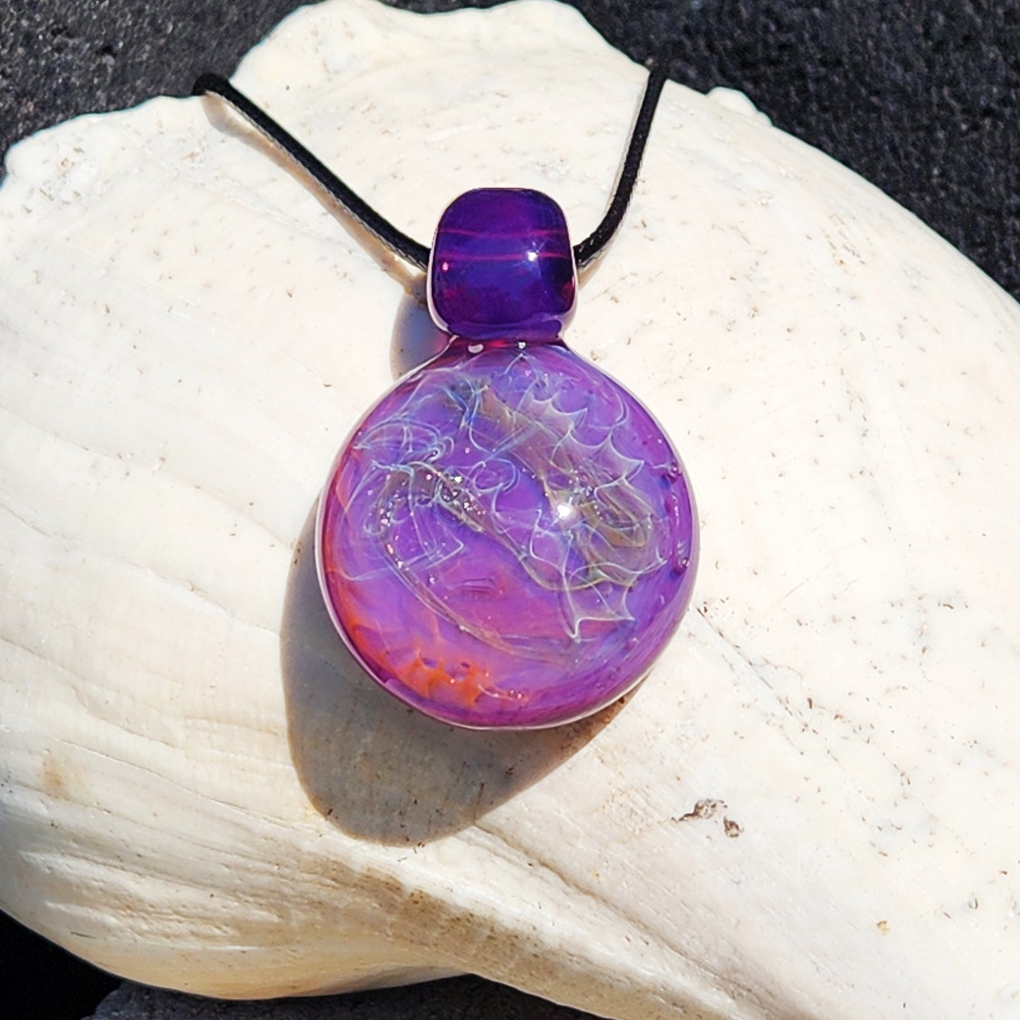 Purple glass pendant necklace resting on a white seashell. Silver and gold fuming create a unique artisan jewelry design.