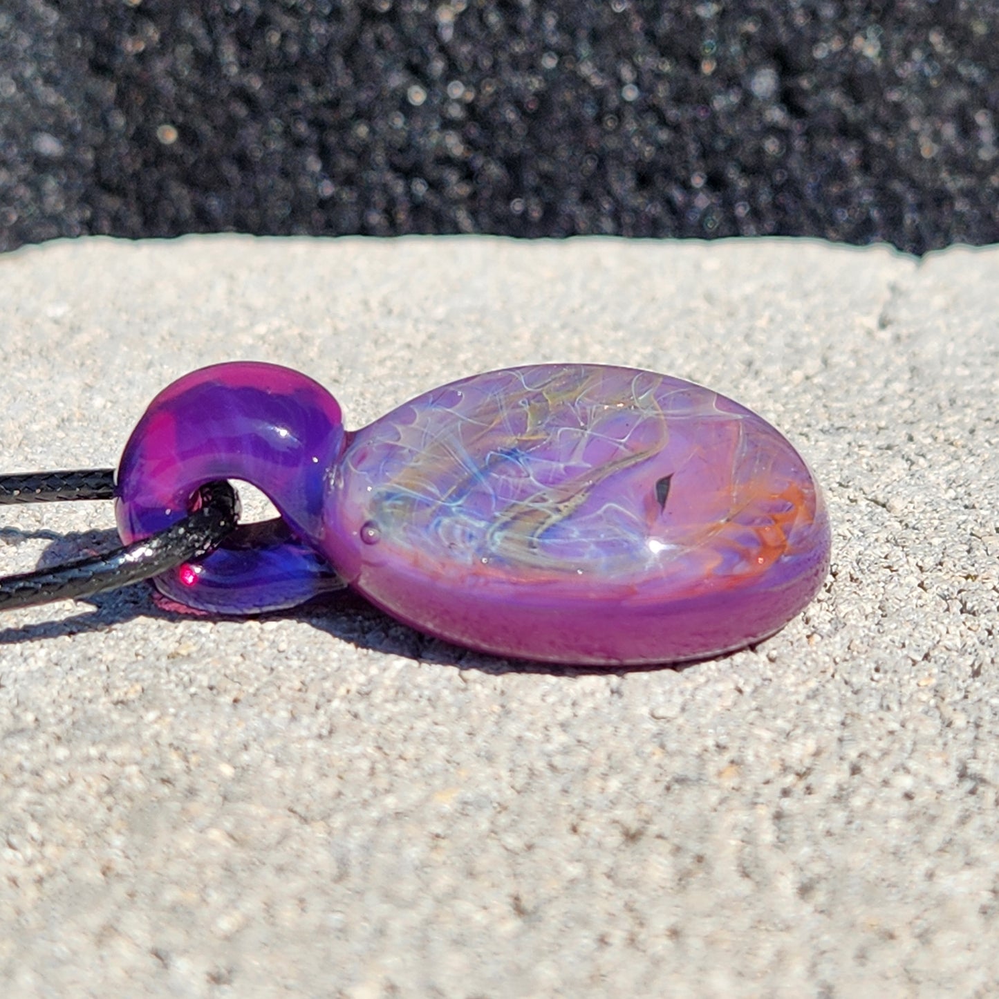 Side view of purple glass pendant with silver and gold fuming. Handcrafted necklace with a smooth, rounded shape and vivid hues.